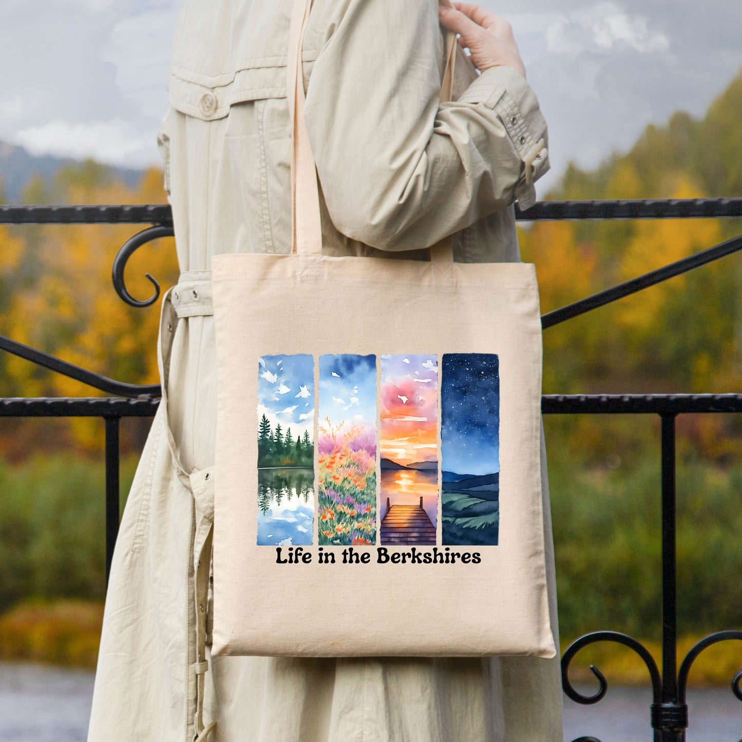Canvas tote bag printed with four seasonal watercolor scenes and the phrase “Life in the Berkshires” in black script modeled over shoulder.