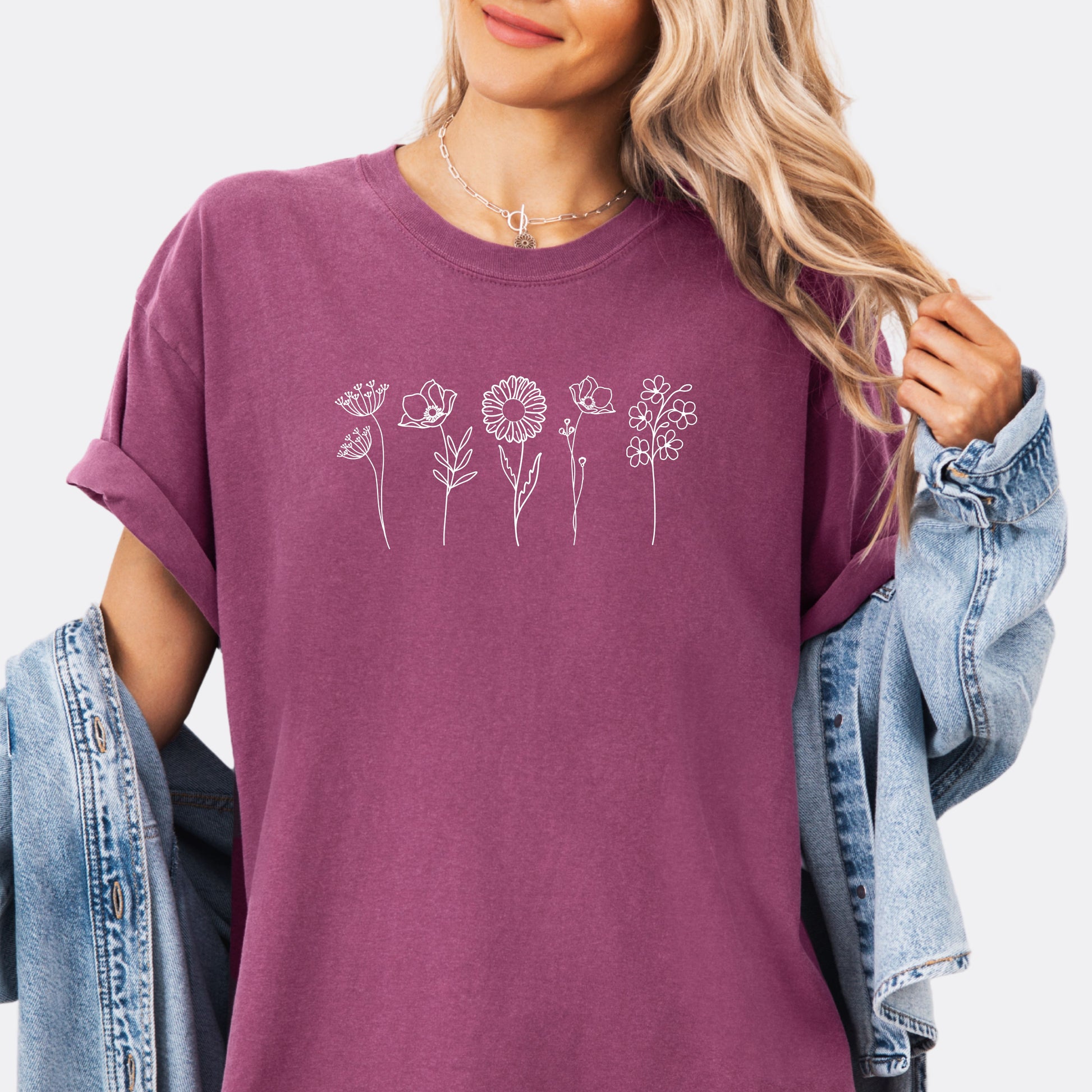 Person wearing a Comfort Colors berry T-shirt featuring a minimalist white line art design of six different wildflowers.
