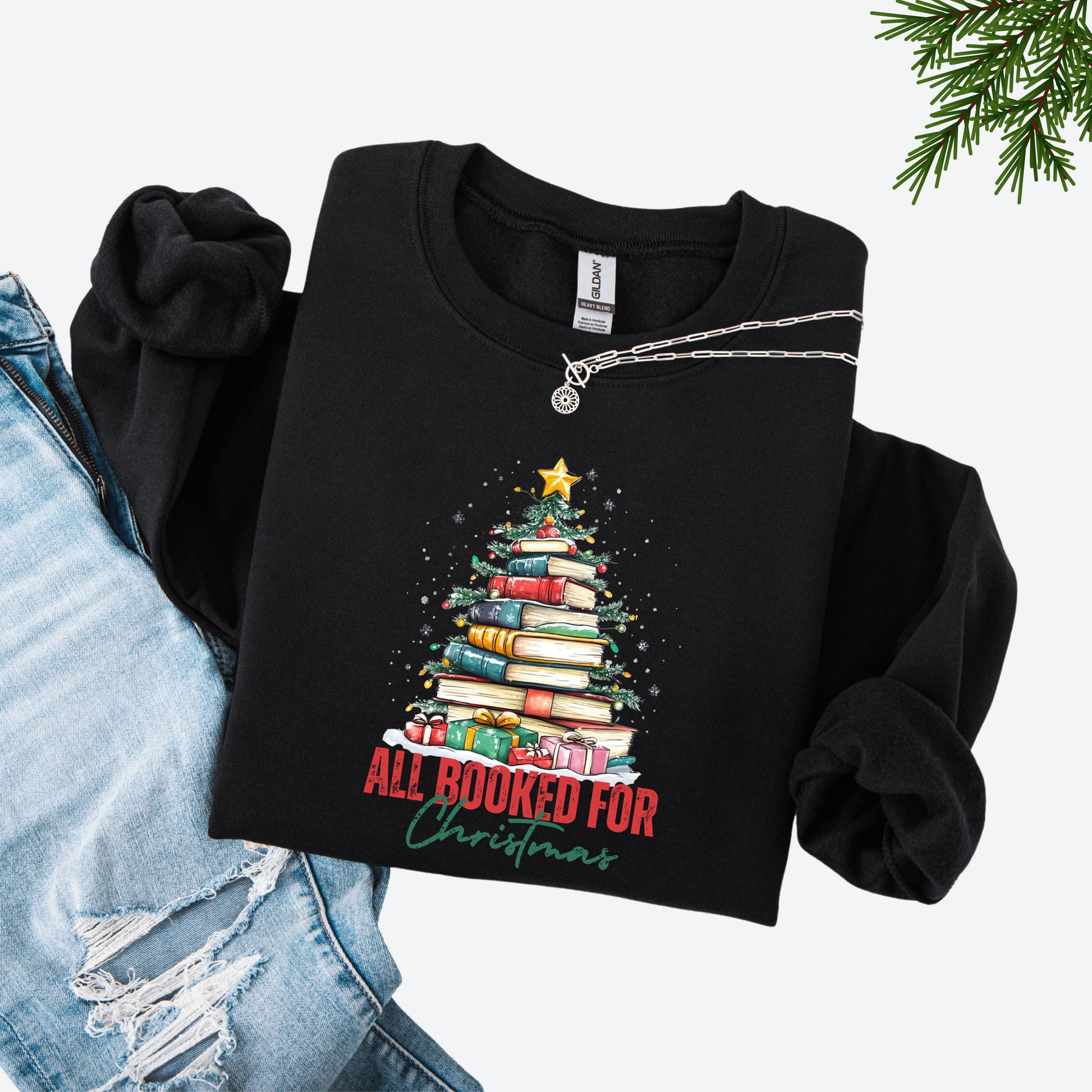 Black crewneck sweatshirt with a holiday design featuring a Christmas tree made of books and the phrase “All Booked For Christmas.”