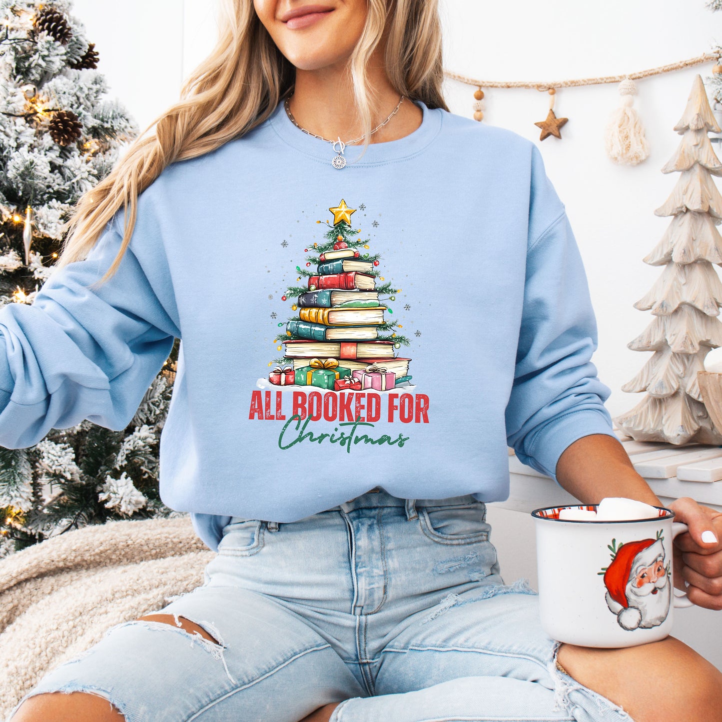 Person wearing a light blue crewneck sweatshirt with a festive Christmas tree made of stacked books and the text “All Booked For Christmas.”