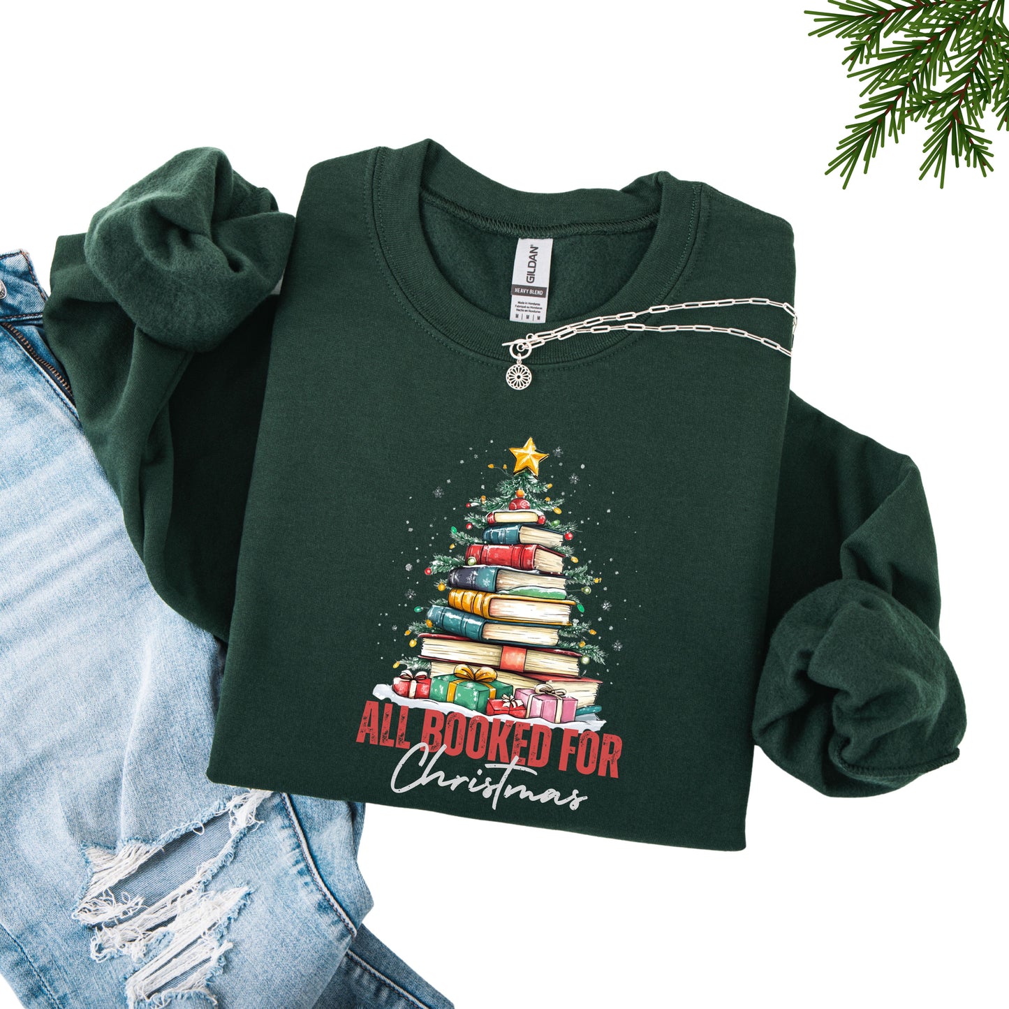 Forest green crewneck sweatshirt with a holiday design featuring a Christmas tree made of books and the phrase “All Booked For Christmas.”