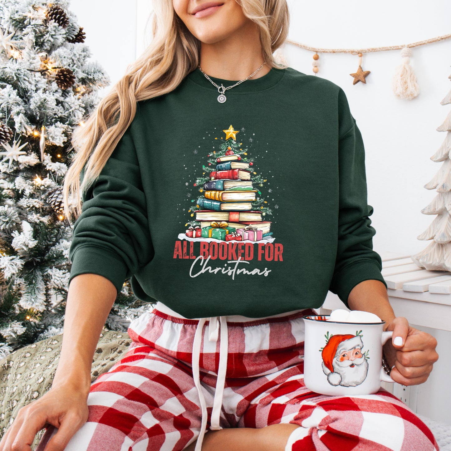Person wearing a forest green crewneck sweatshirt with a festive Christmas tree made of stacked books and the text “All Booked For Christmas.”