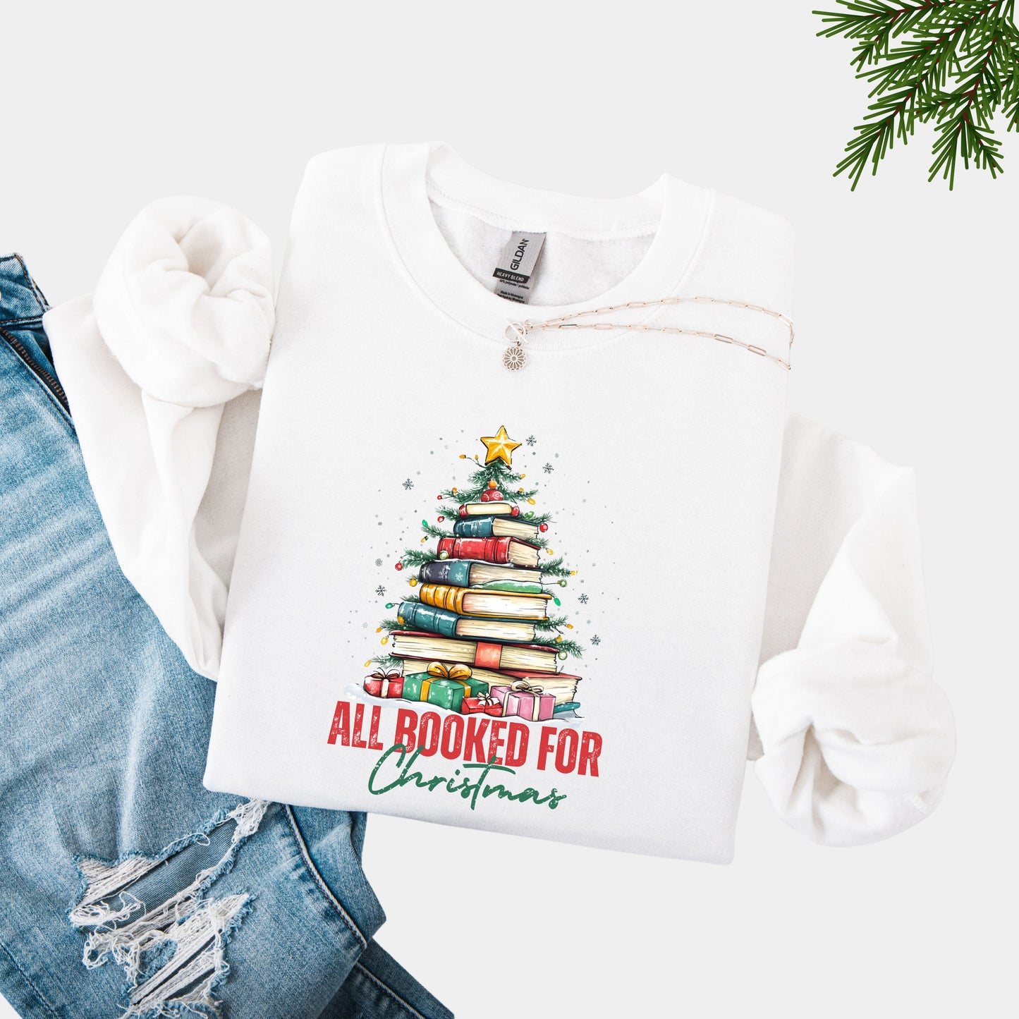 White crewneck sweatshirt with a holiday design featuring a Christmas tree made of books and the phrase “All Booked For Christmas.”