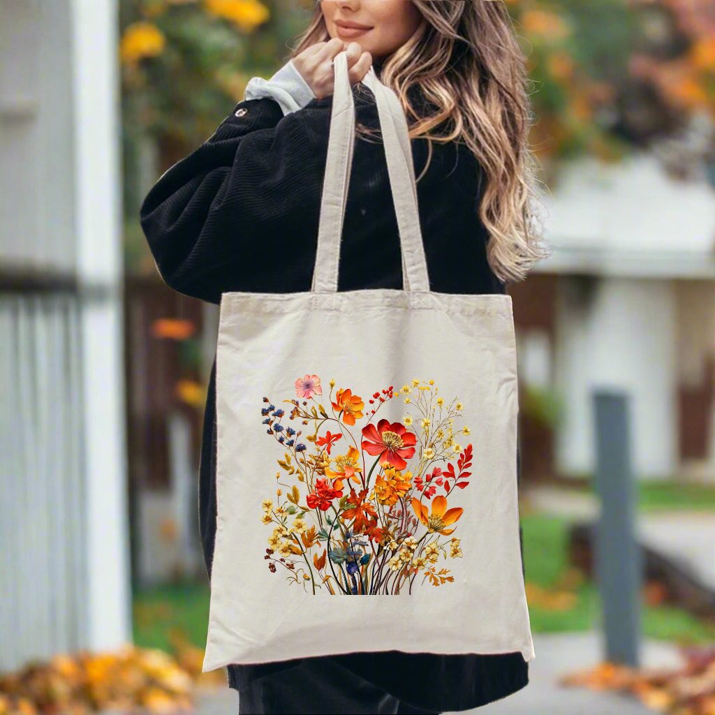 Woman carrying a cotton canvas tote bag with a printed bouquet of autumn wildflowers in warm fall tones.