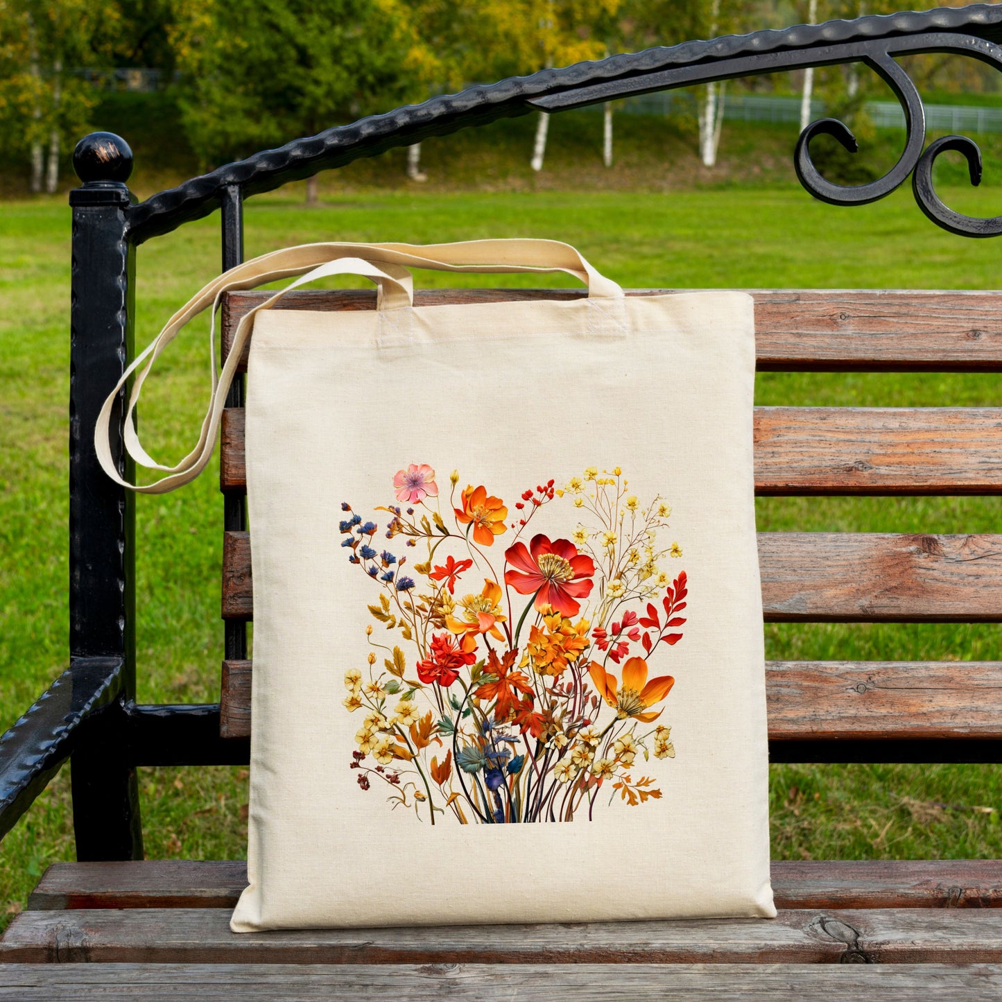 Cotton canvas tote bag with a printed bouquet of autumn wildflowers in warm fall tones on bench.