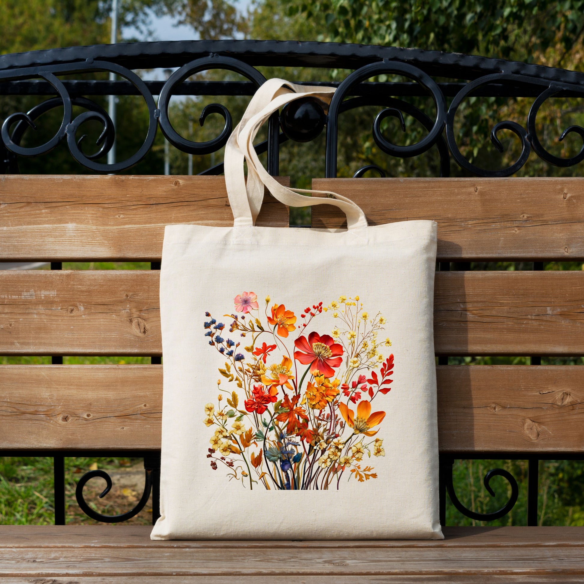 Cotton canvas tote bag with a printed bouquet of autumn wildflowers in warm fall tones on bench.