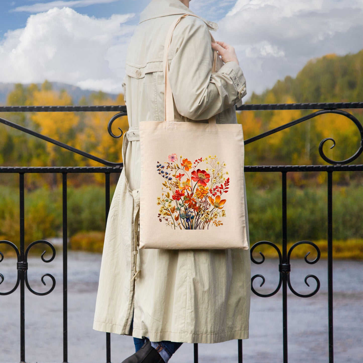 Woman carrying a cotton canvas tote bag with a printed bouquet of autumn wildflowers in warm fall tones.