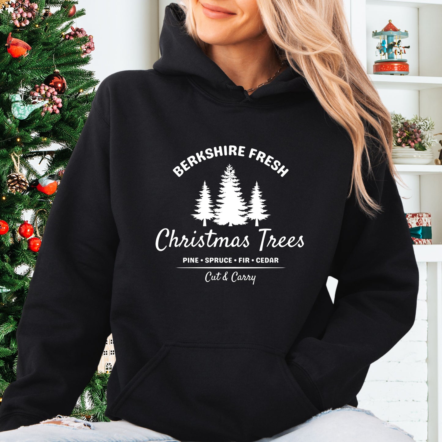 Model wearing black Berkshire Fresh Christmas Trees hoodie with holiday tree farm graphic on the front