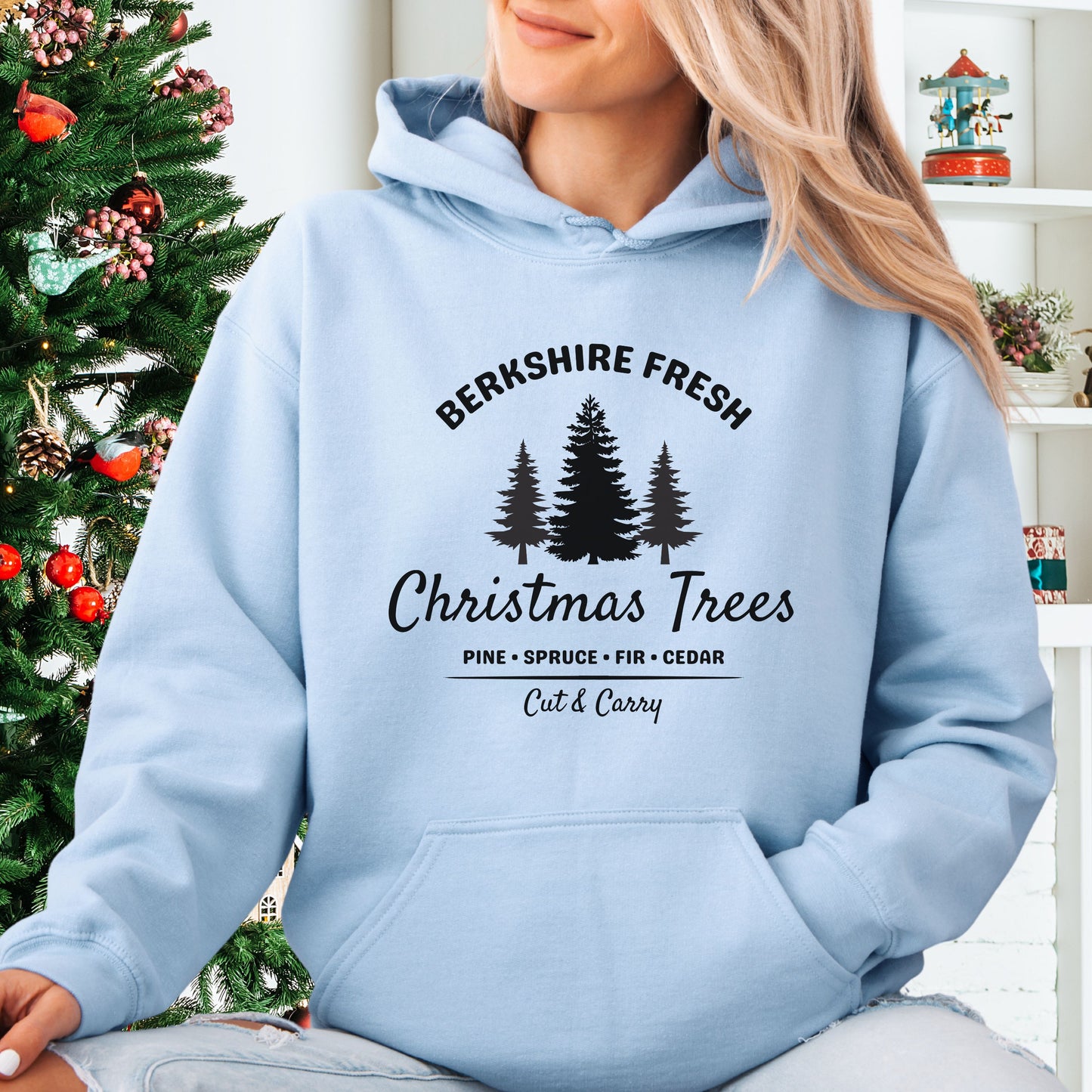 Model wearing light blue Berkshire Fresh Christmas Trees hoodie with holiday tree farm graphic on the front