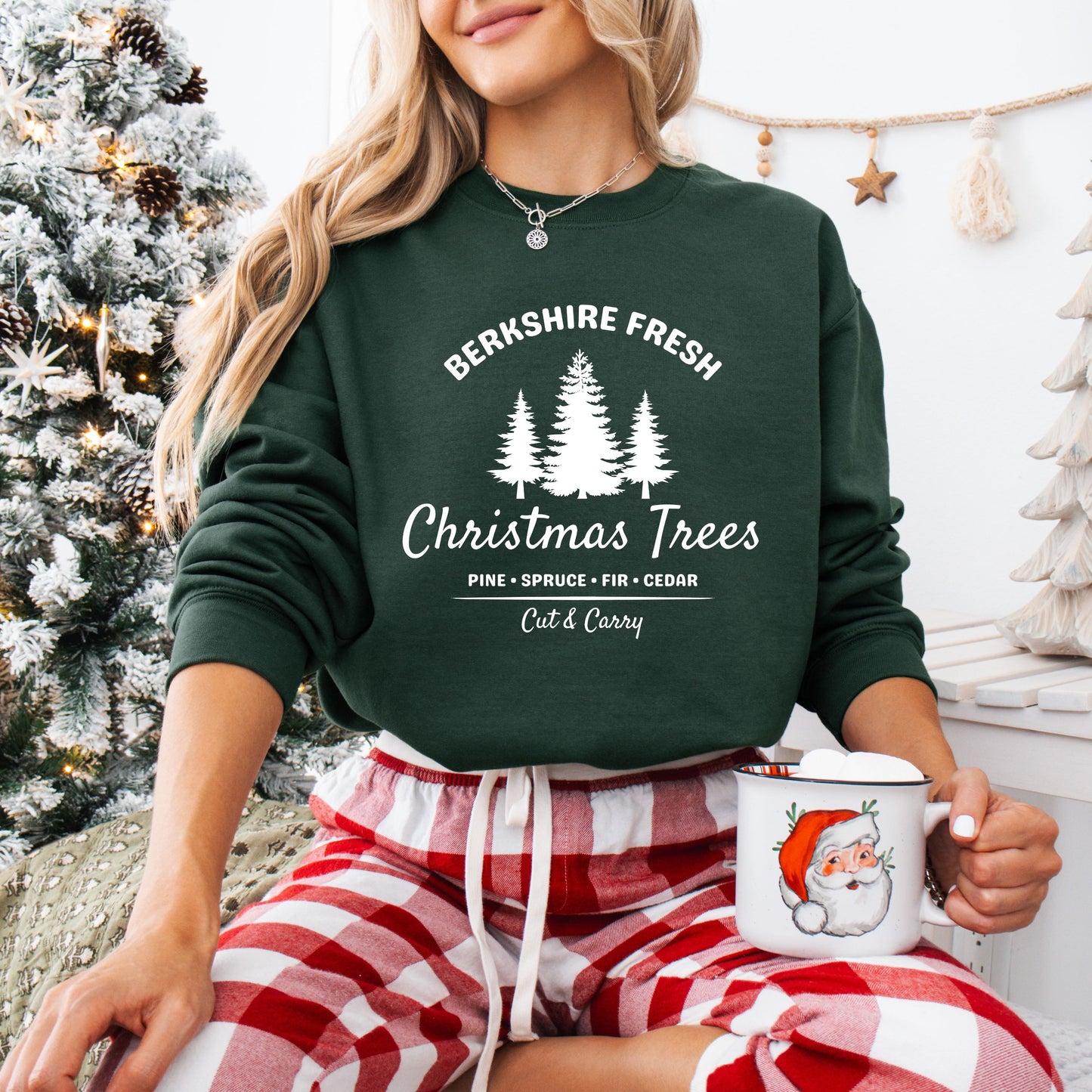 Person wearing a green 'Berkshire Fresh Christmas Trees' sweatshirt with white text and trees graphic and holiday themed background.