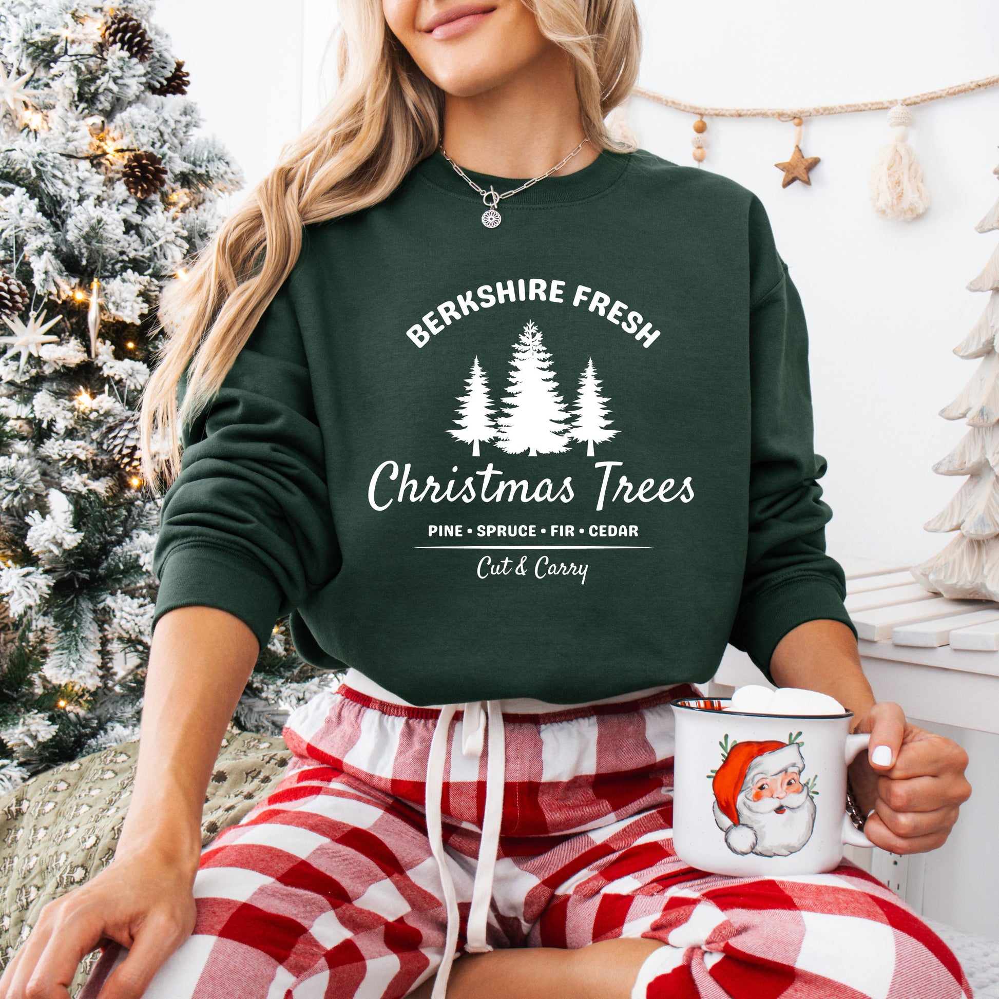 Person wearing a green 'Berkshire Fresh Christmas Trees' sweatshirt with white text and trees graphic and holiday themed background.