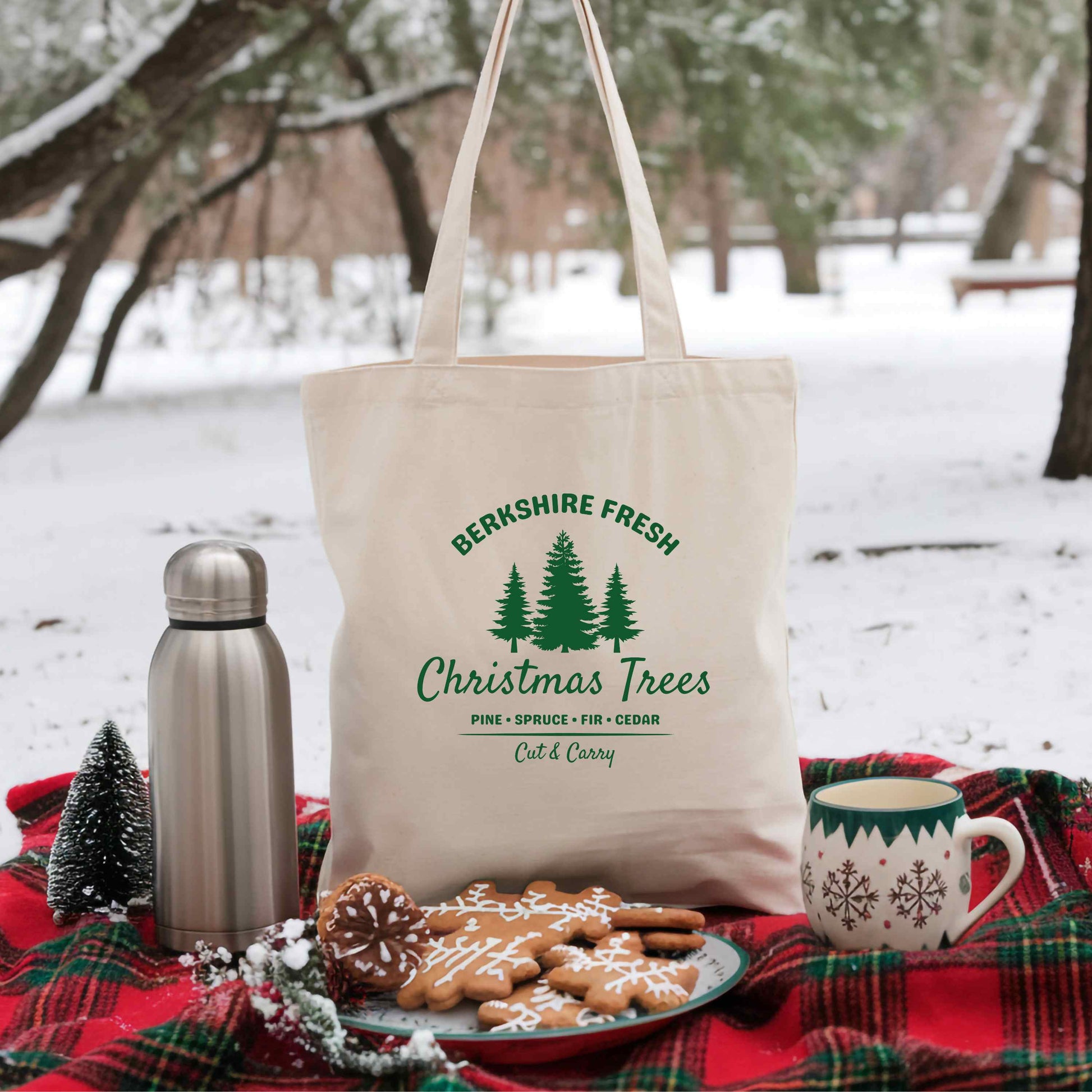 Tote bag with 'Berkshire Fresh Christmas Trees' design on a snowy outdoor setting with cookies and a mug.