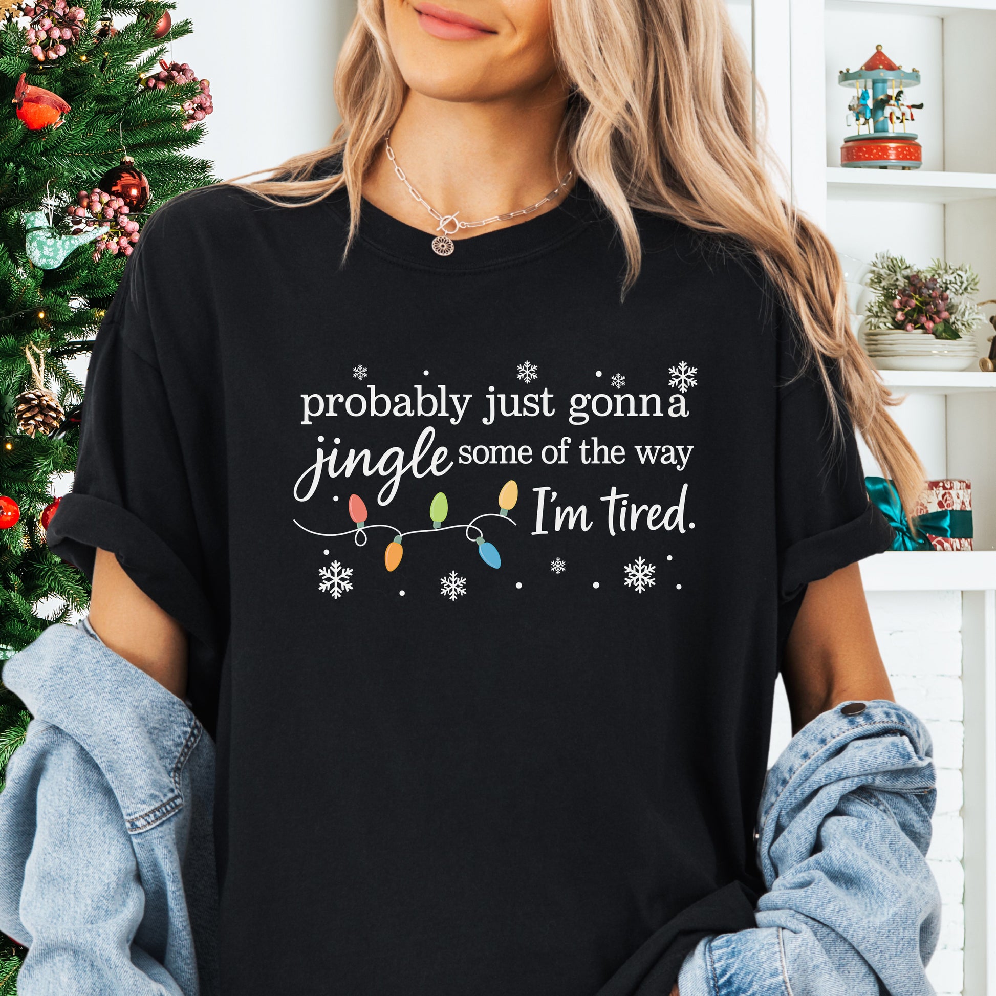 Person wearing black comfort colors shirt with colorful Christmas lights and funny text that says probably just gonna jingle some of the way I’m tired