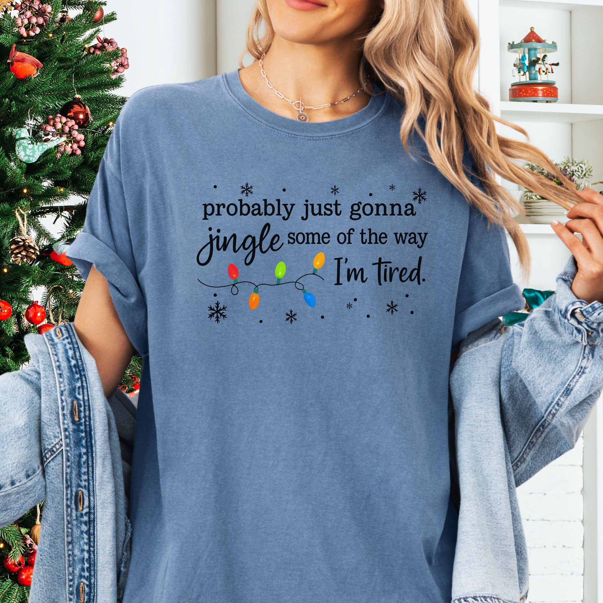 Person wearing blue jean comfort colors shirt with colorful Christmas lights and funny text that says probably just gonna jingle some of the way I’m tired