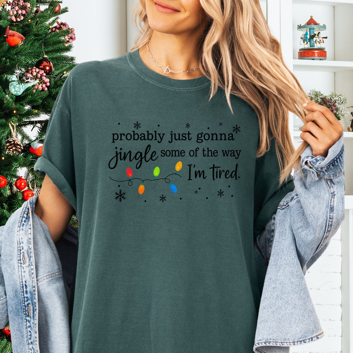 Person wearing blue spruce comfort colors shirt with colorful Christmas lights and funny text that says probably just gonna jingle some of the way I’m tired