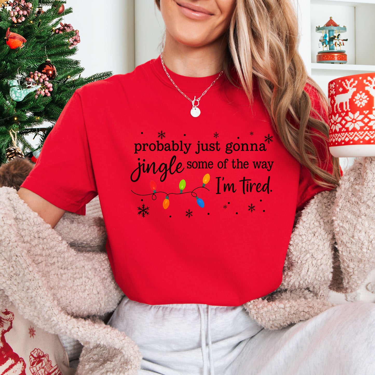 Person wearing red comfort colors shirt with colorful Christmas lights and funny text that says probably just gonna jingle some of the way I’m tired