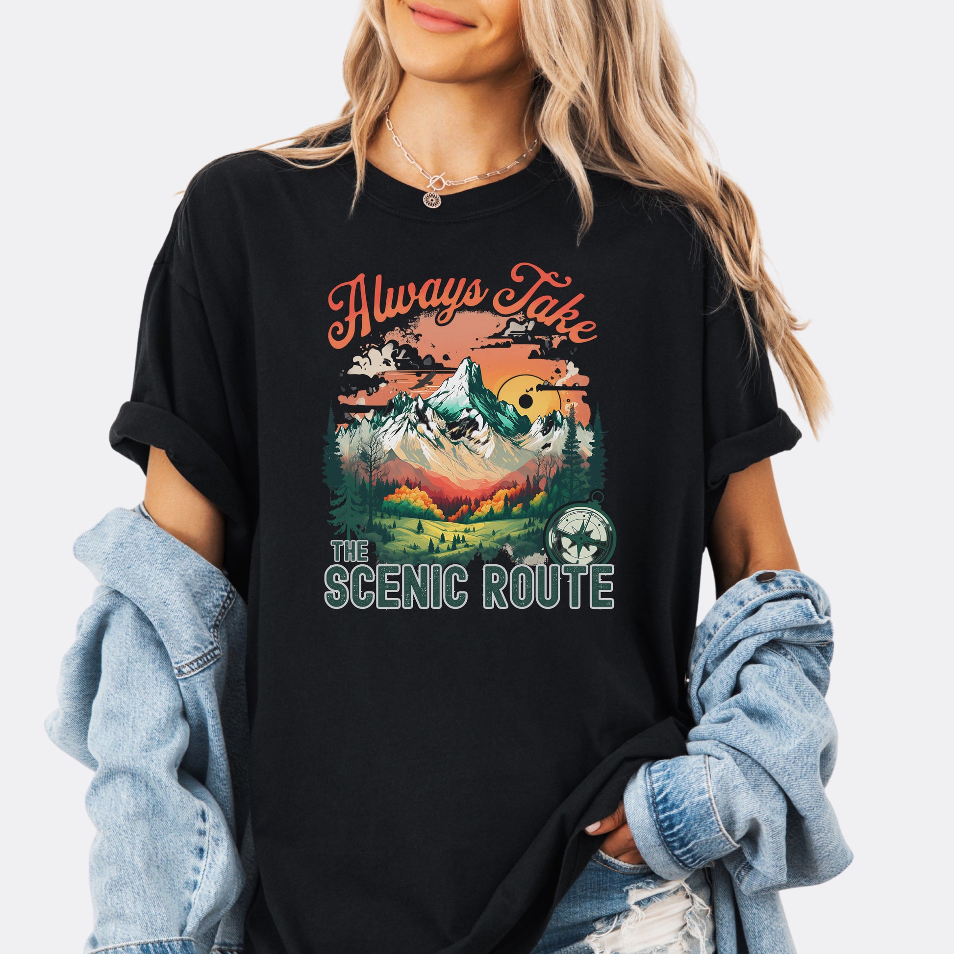 Person wearing a Comfort Colors T-shirt  in the color Black with a nature-inspired “Always Take the Scenic Route” design on the front.