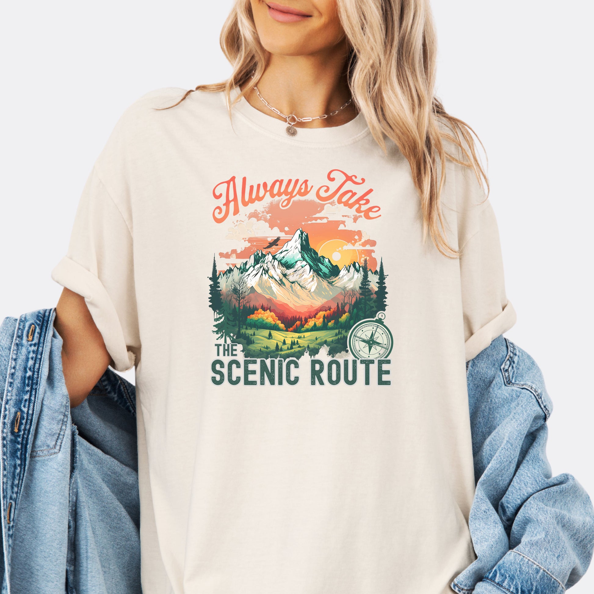 Person wearing a Comfort Colors T-shirt  in the color Ivory with a nature-inspired “Always Take the Scenic Route” design on the front.