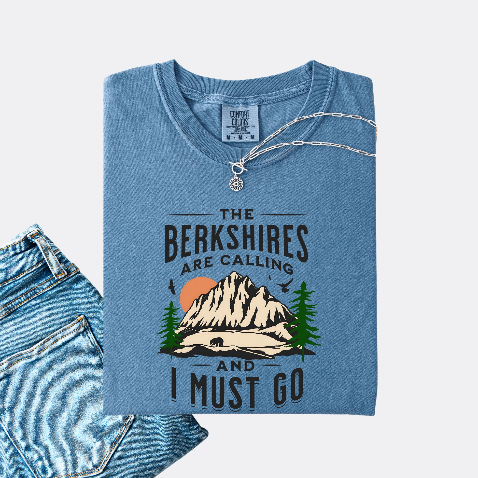 Comfort Colors 1717 T-shirt in blue jean. Shirt features a graphic design of mountains, pine trees, and a bear with the text ‘The Berkshires are calling and I must go.’”