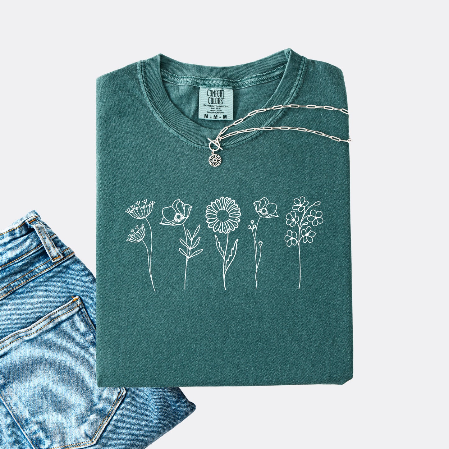 Comfort Colors blue spruce T-shirt featuring a minimalist white line art design of six different wildflowers.