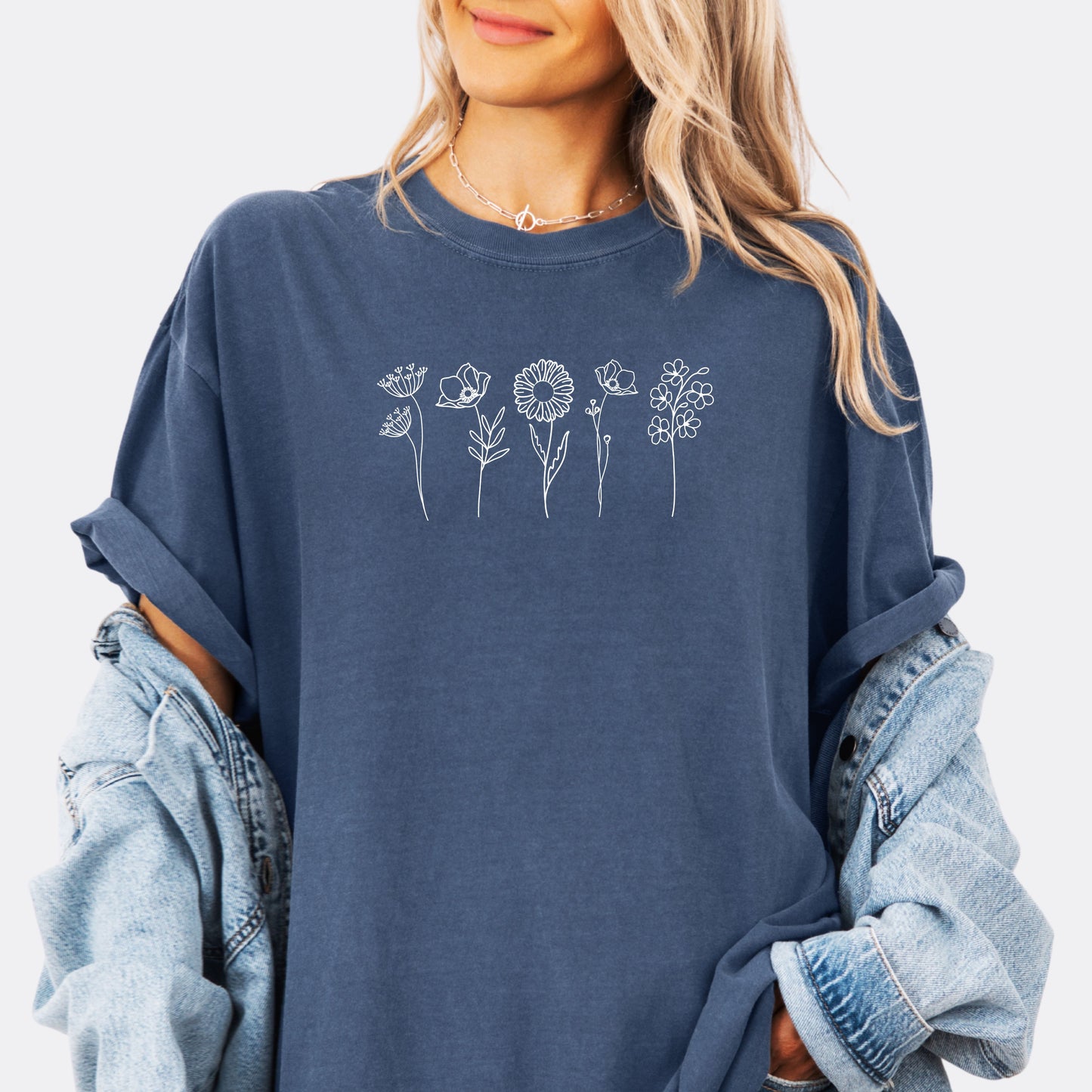 Person wearing a Comfort Colors denim T-shirt featuring a minimalist white line art design of six different wildflowers.