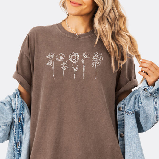 Person wearing a Comfort Colors expresso T-shirt featuring a minimalist white line art design of six different wildflowers.