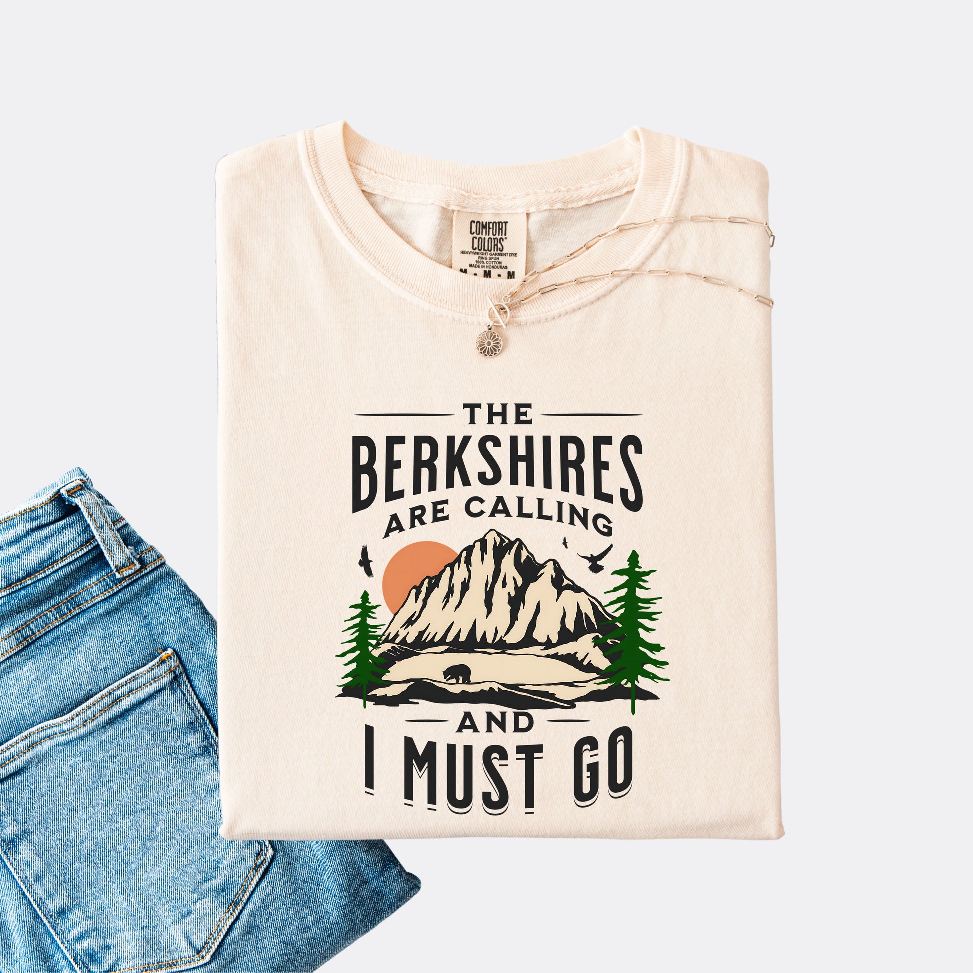 Comfort Colors 1717 T-shirt in the color ivory. Shirt features a graphic design of mountains, pine trees, and a bear with the text ‘The Berkshires are calling and I must go.’”