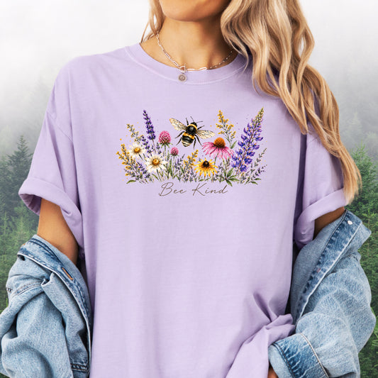 Person wearing Bee Kind Comfort Colors t-shirt with watercolor bee and wildflowers in the color orchard.