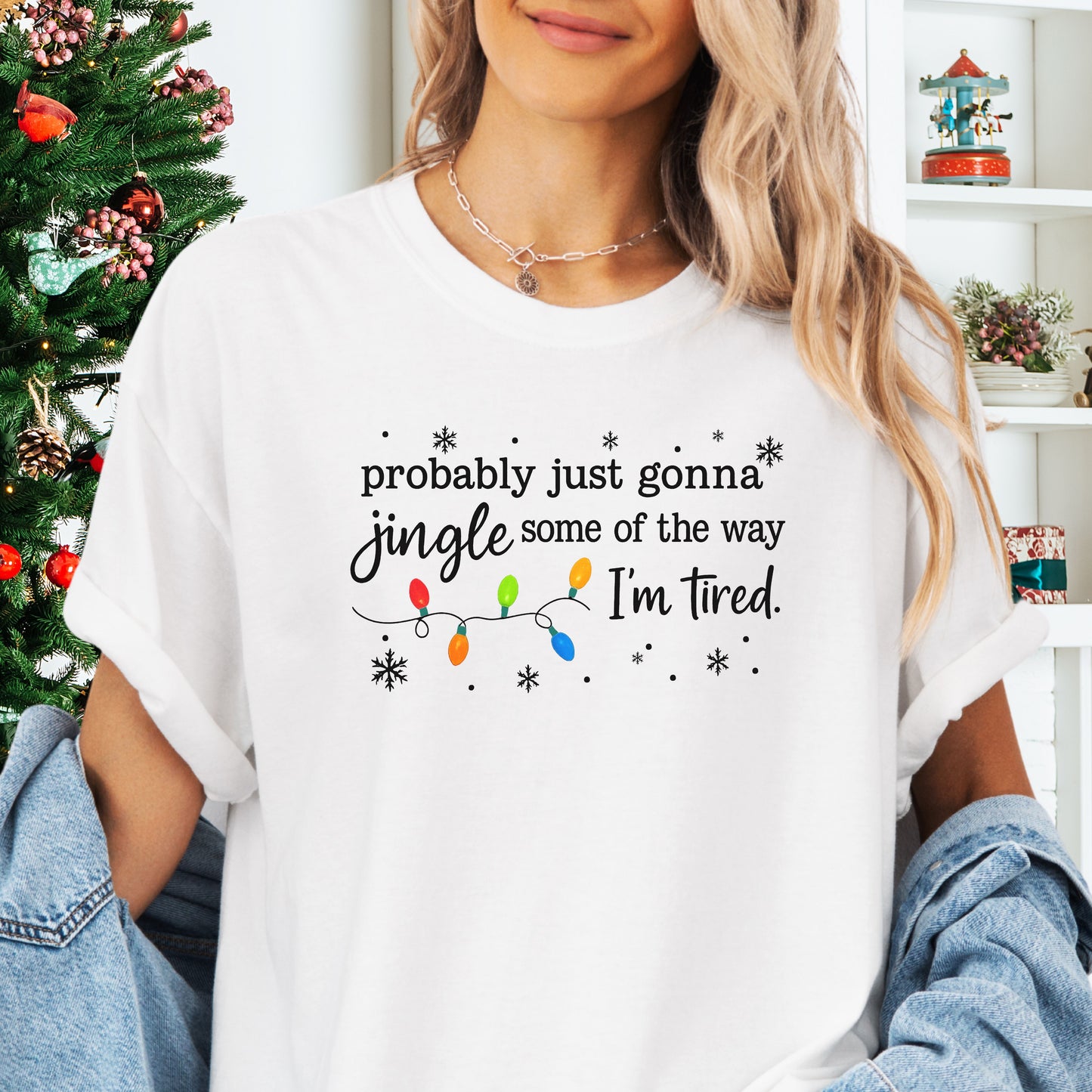 Person wearing white comfort colors shirt with colorful Christmas lights and funny text that says probably just gonna jingle some of the way I’m tired