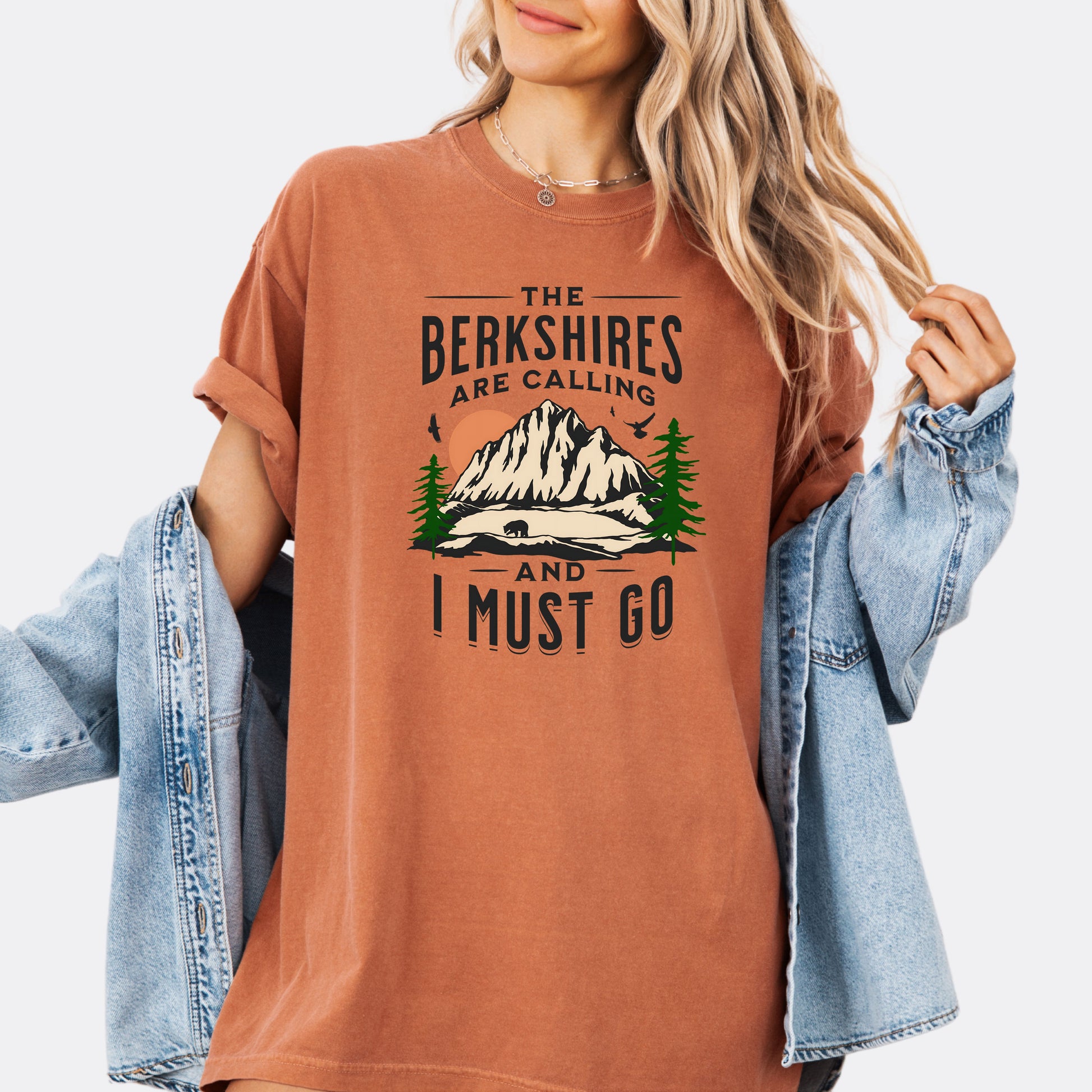Person wearing Comfort Colors 1717 T-shirt in the color yam. Shirt features a graphic design of mountains, pine trees, and a bear with the text ‘The Berkshires are calling and I must go.’”