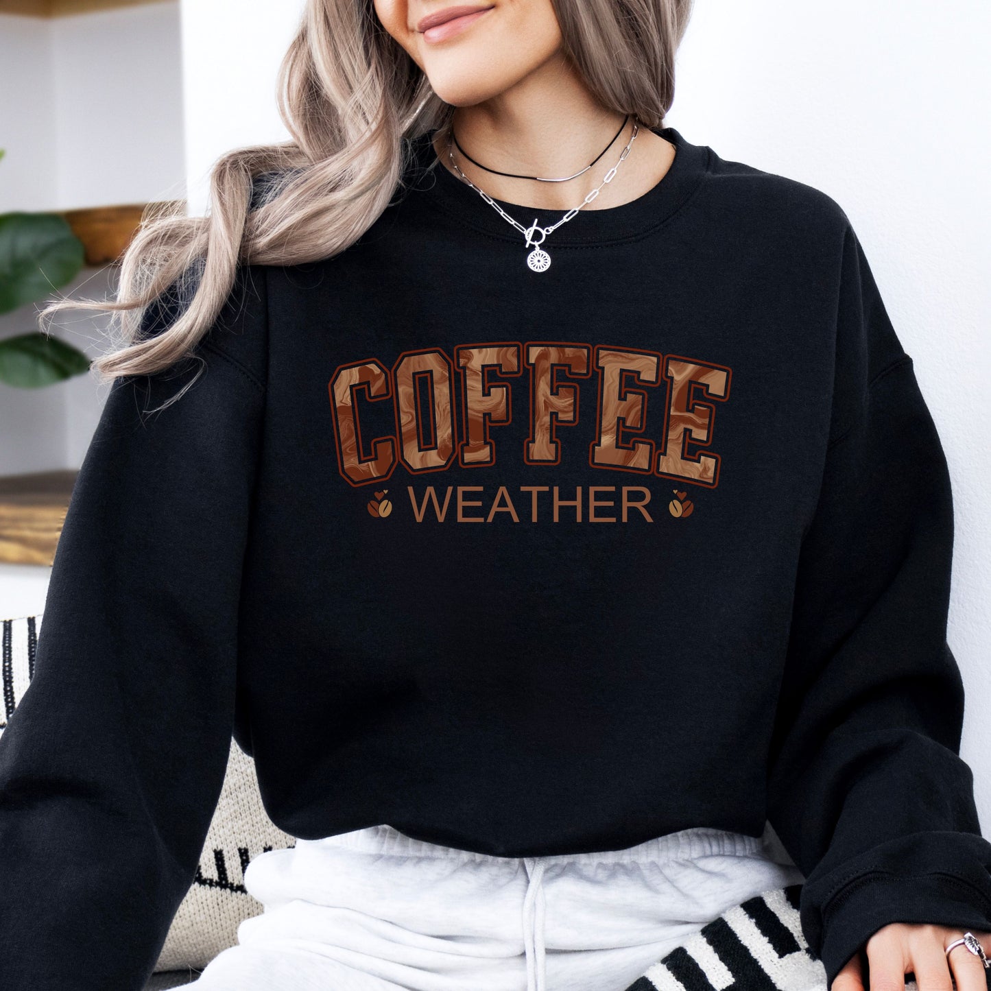 Person wearing coffee weather sweatshirt with marbled brown lettering and coffee bean icons on black crewneck.