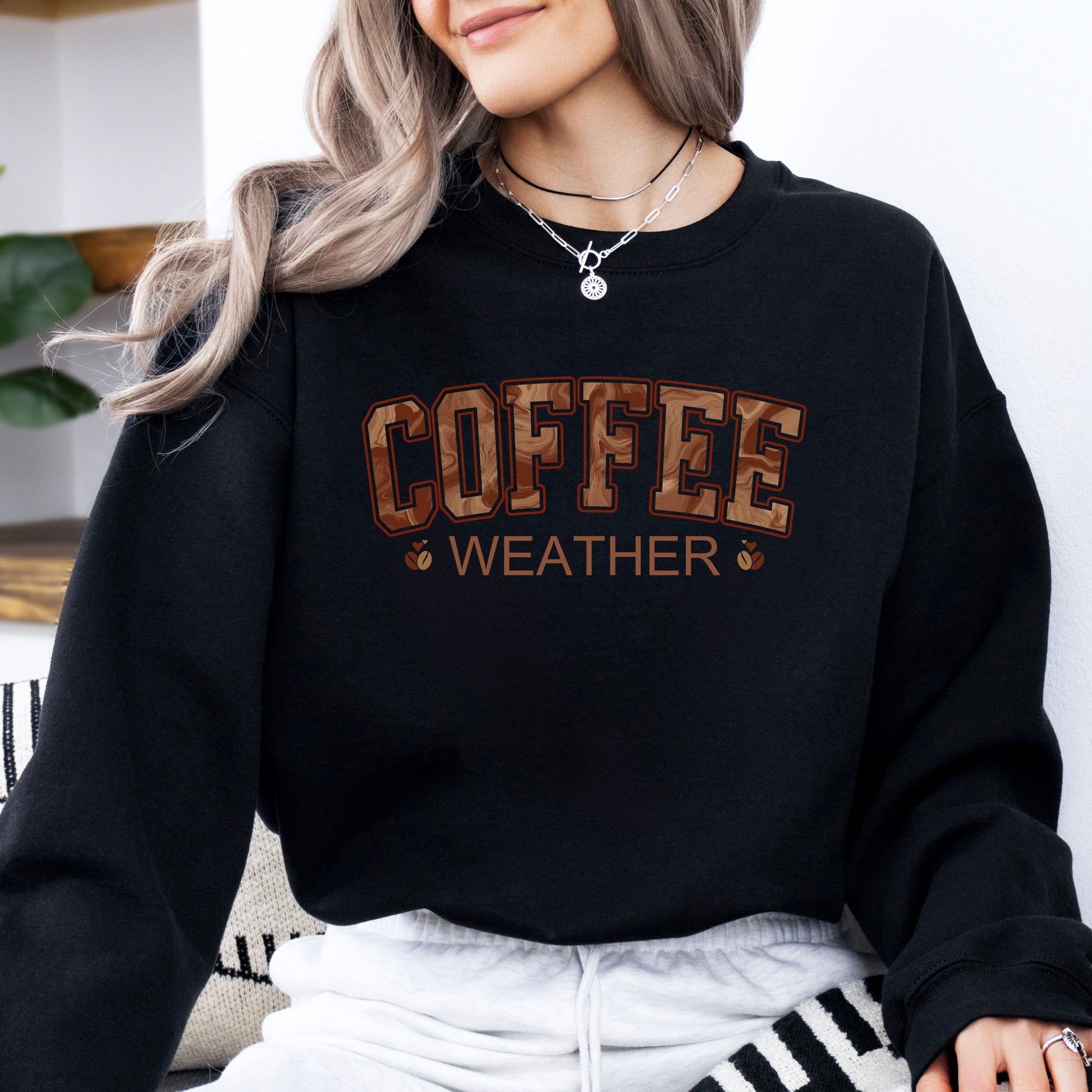 Person wearing coffee weather sweatshirt with marbled brown lettering and coffee bean icons on black crewneck.