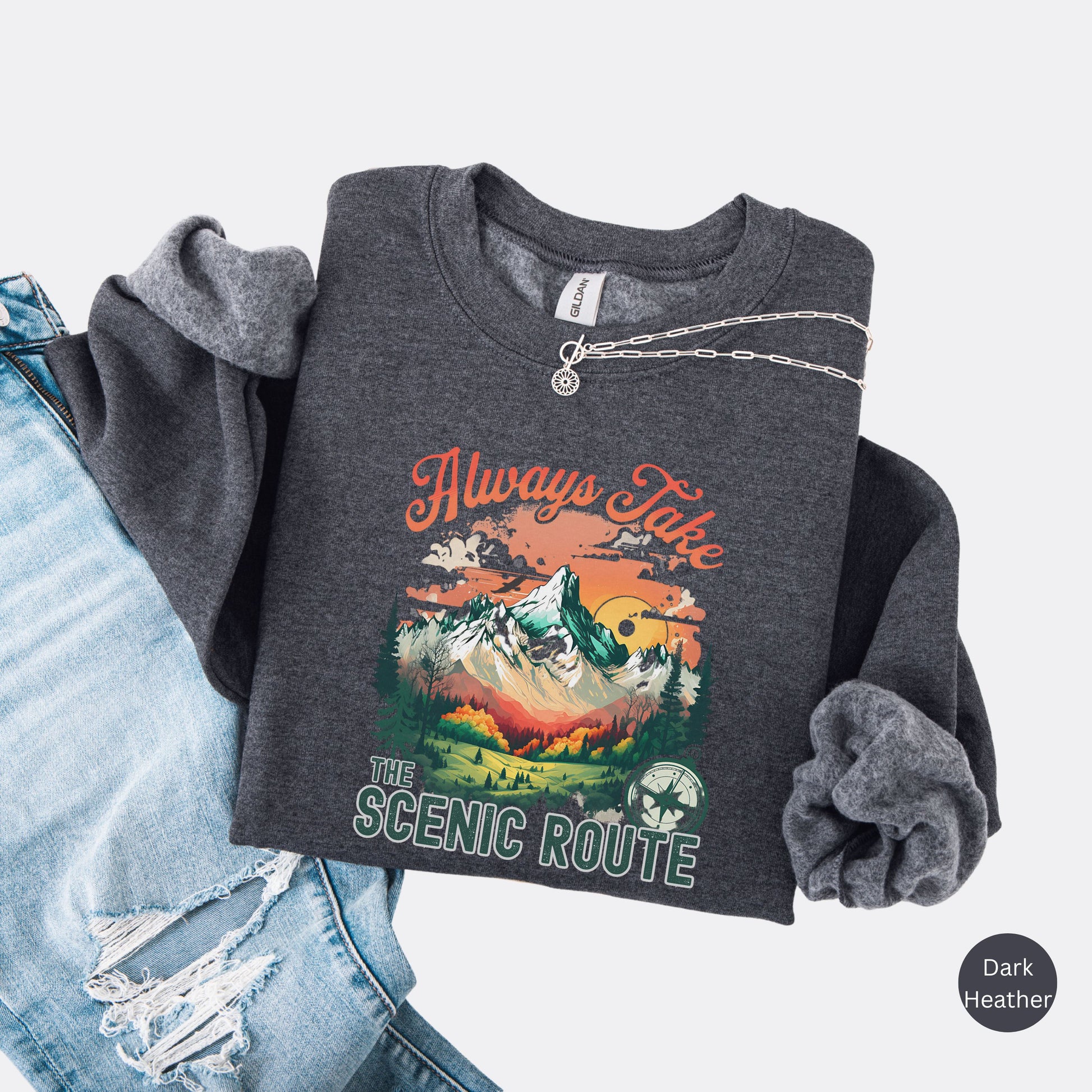 Crewneck sweatshirt in the color dark heather with the phrase “Always Take the Scenic Route” and a mountain-inspired graphic on the front.