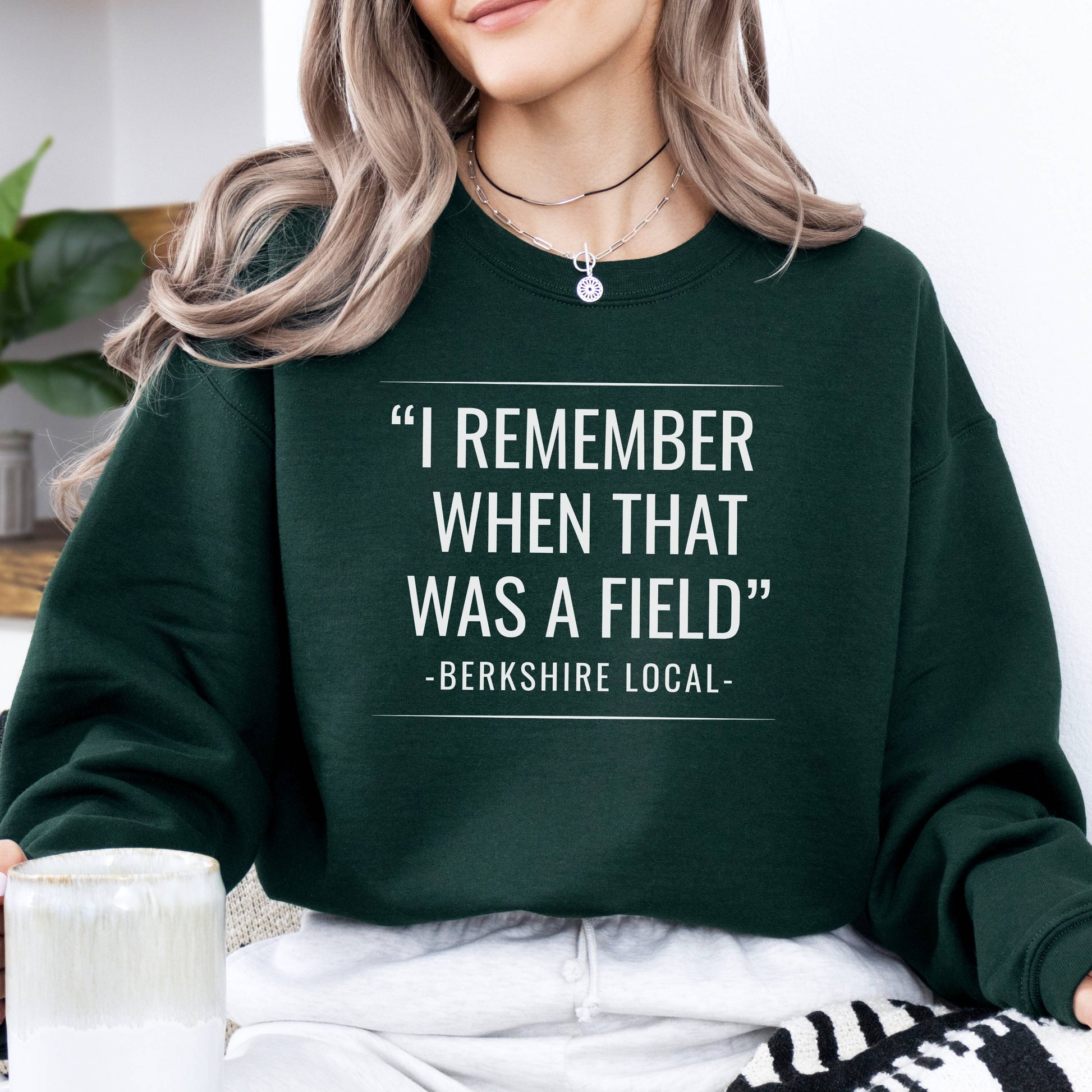 Person wearing sweatshirt with the quote "I remember when that was a field" -Berkshire Local-, in the color forest green