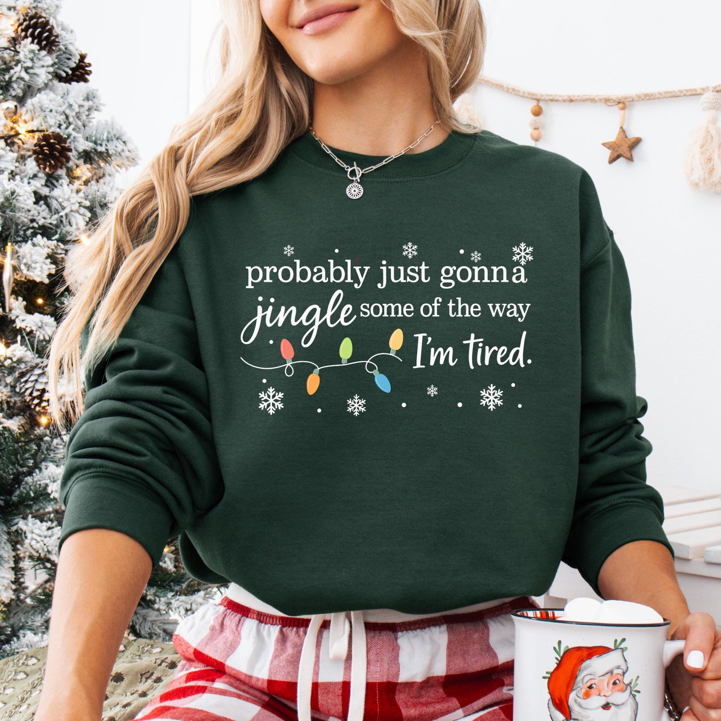 Person wearing a forest green sweatshirt with Christmas lights and the text "probably just gonna jingle some of the way I'm tired".