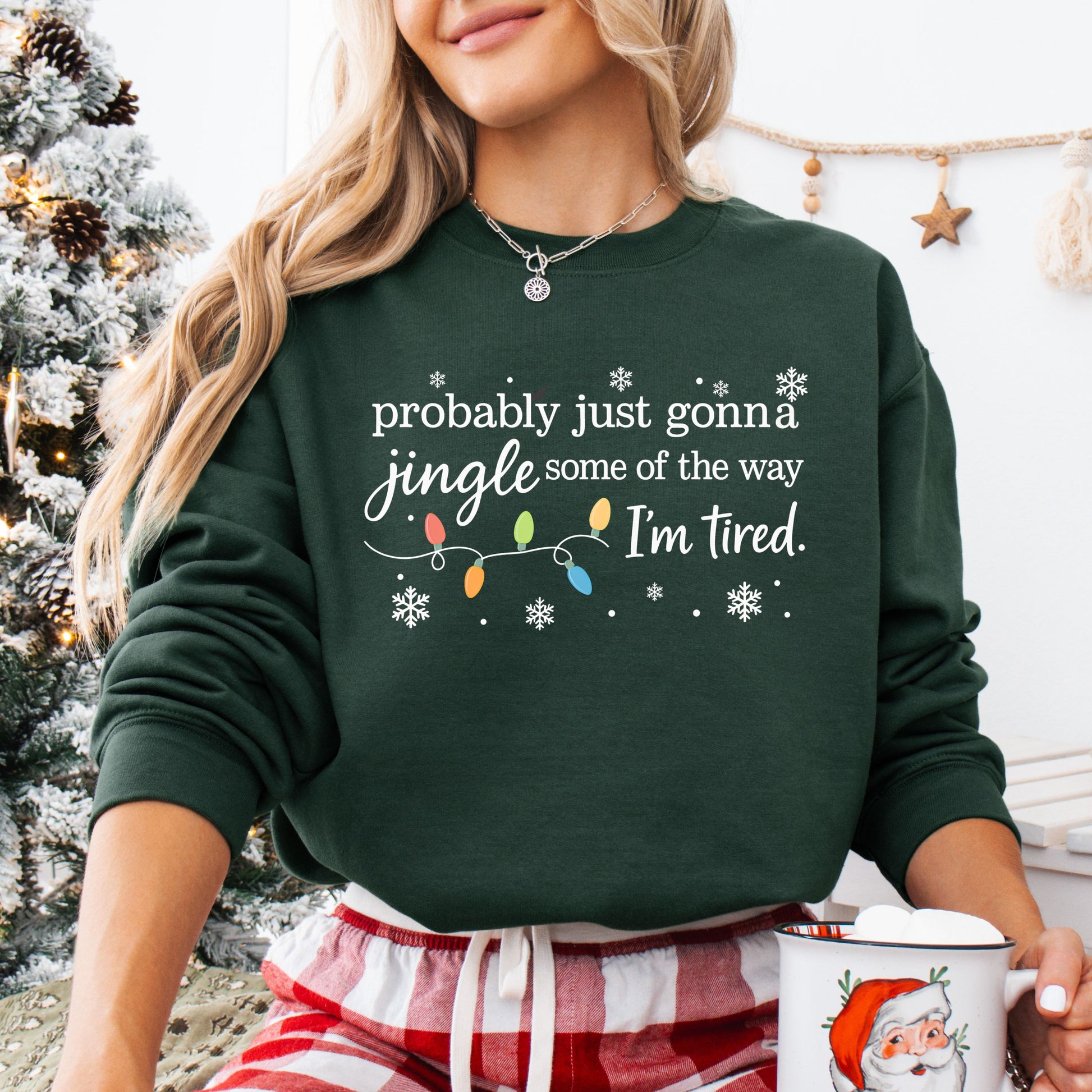 Person wearing a forest green sweatshirt with Christmas lights and the text "probably just gonna jingle some of the way I'm tired".