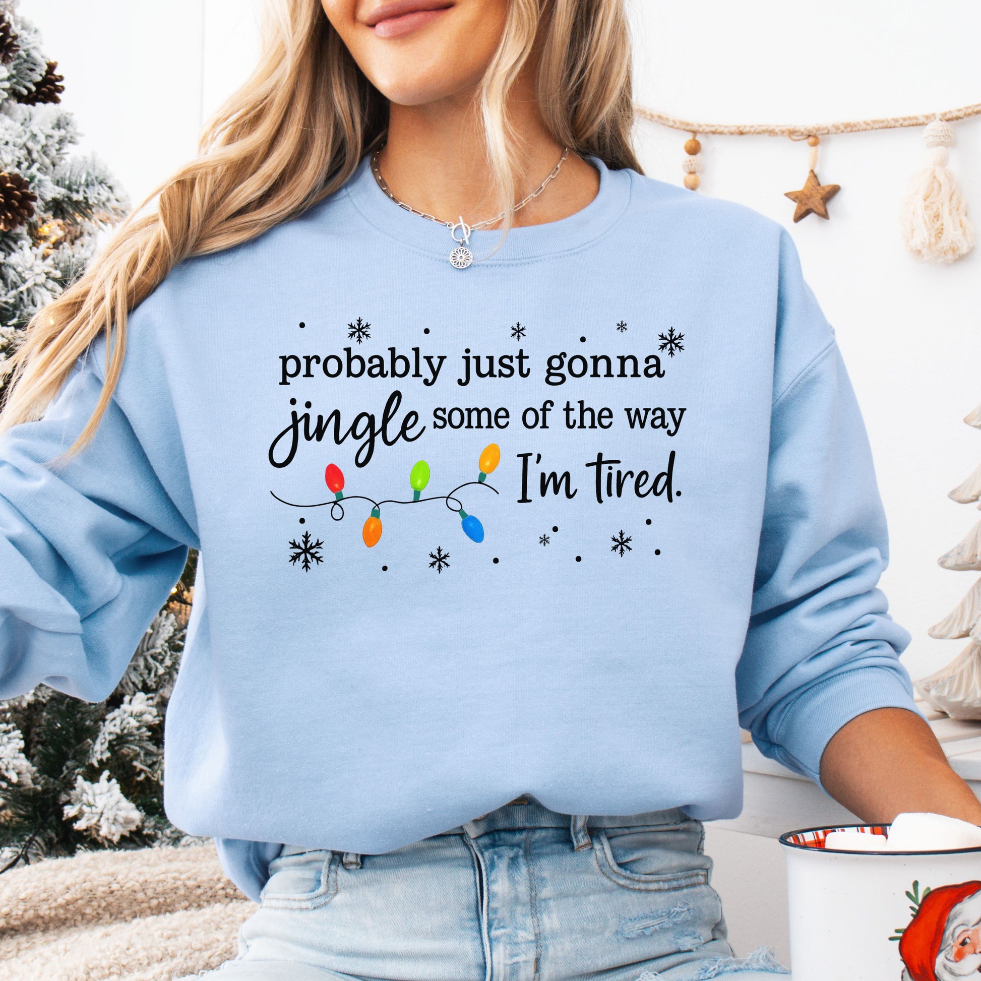 Person wearing a light blue sweatshirt with Christmas lights and the text "probably just gonna jingle some of the way I'm tired".