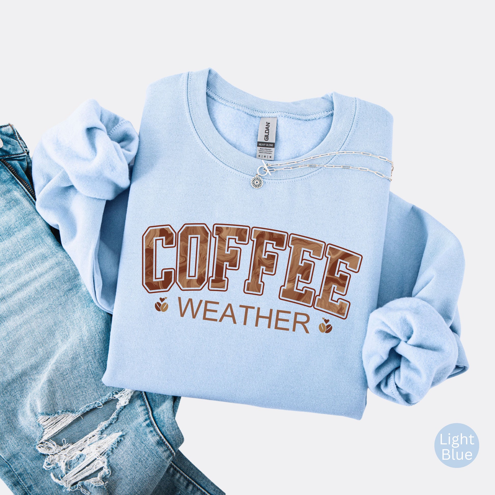 Coffee weather sweatshirt with marbled brown lettering and coffee bean icons on light blue  crewneck.