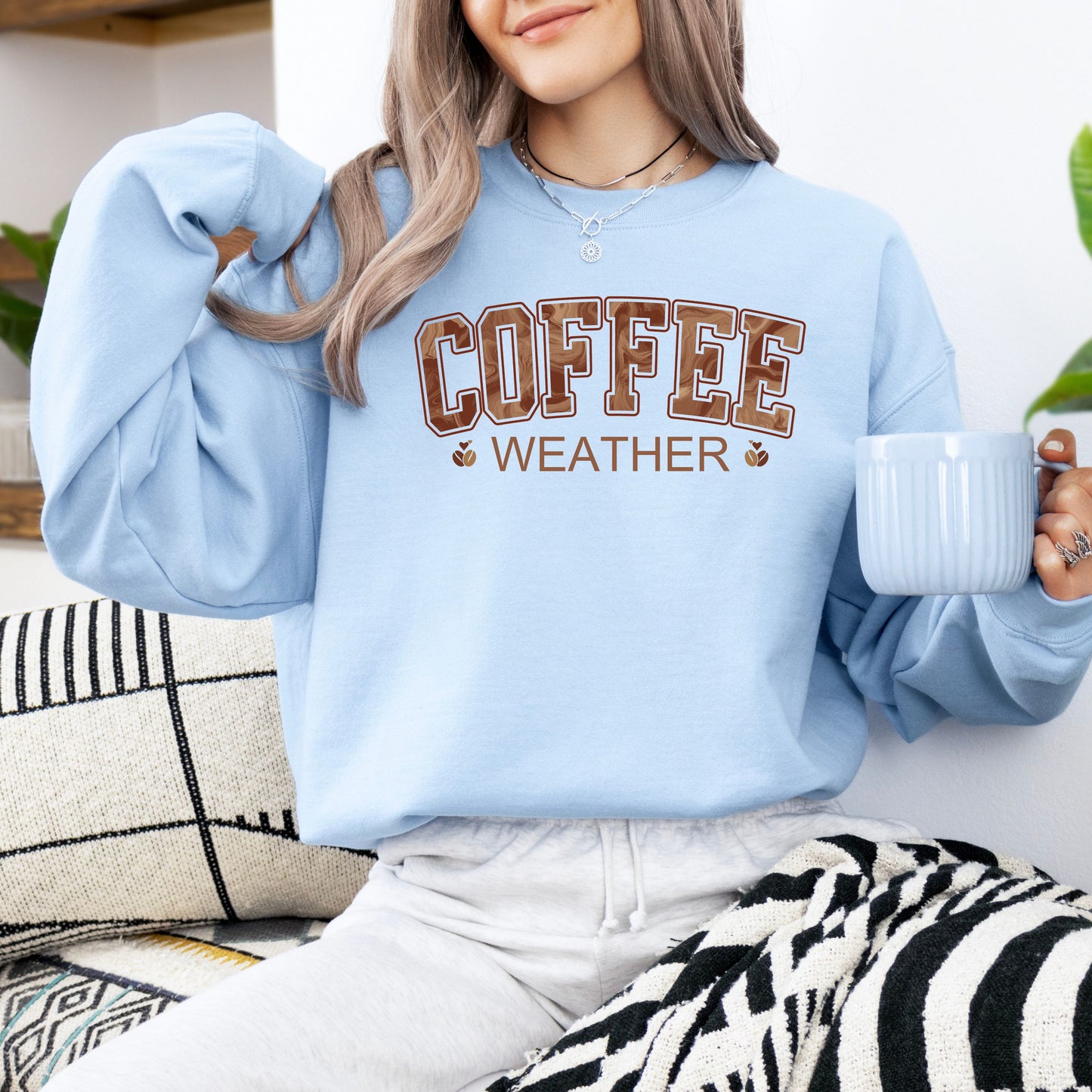 Person wearing coffee weather sweatshirt with marbled brown lettering and coffee bean icons on light blue  crewneck.