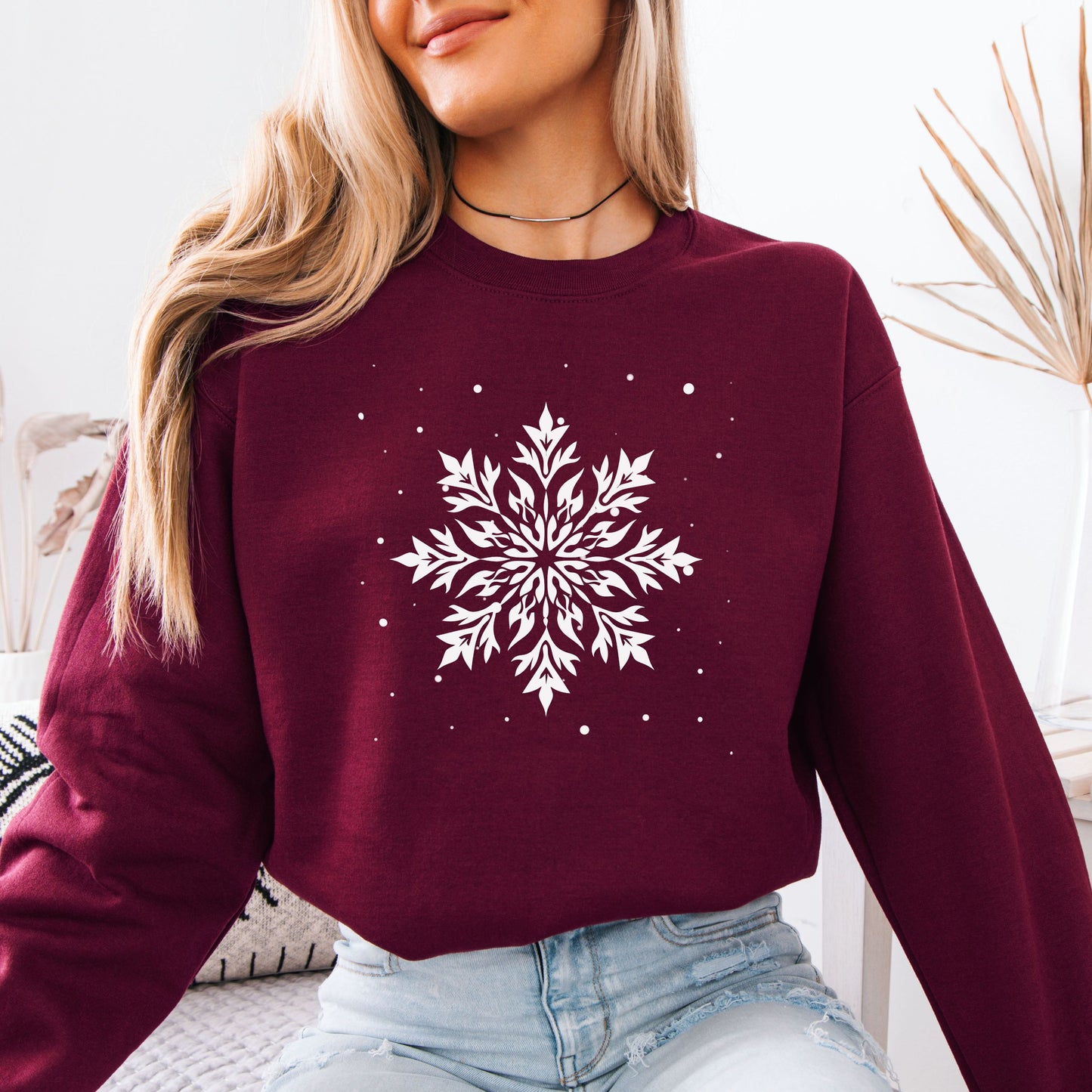 Person wearing snowflake design with falling snow on cozy unisex winter sweatshirt in the color maroon