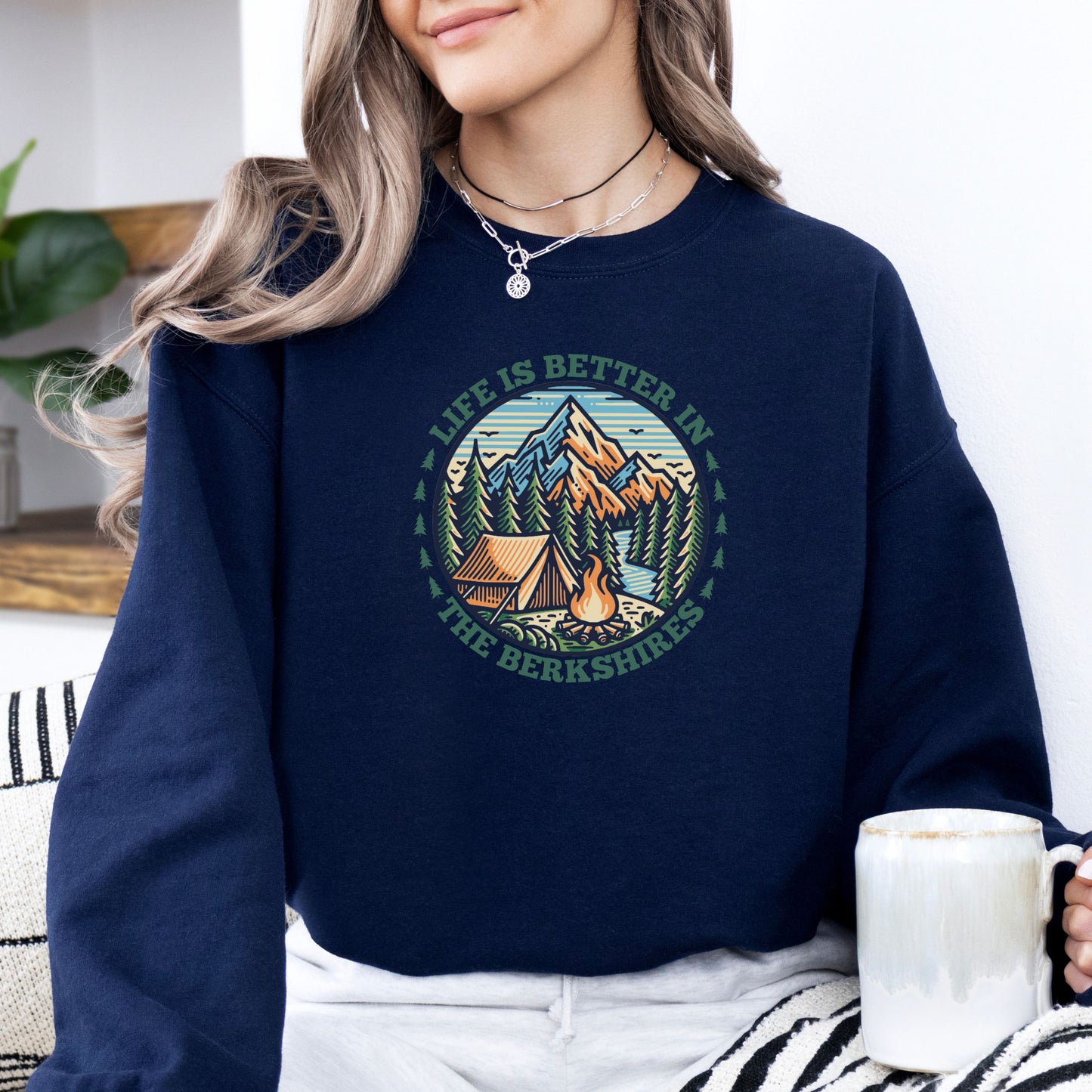 Person wearing a navy sweatshirt with mountain scene pine trees tent and campfire graphic with the text Life Is Better In The Berkshires