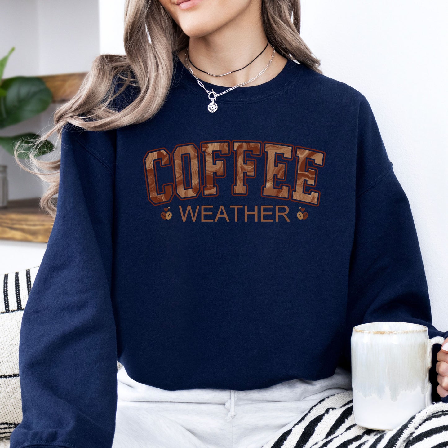 Person wearing coffee weather sweatshirt with marbled brown lettering and coffee bean icons on navy  crewneck.