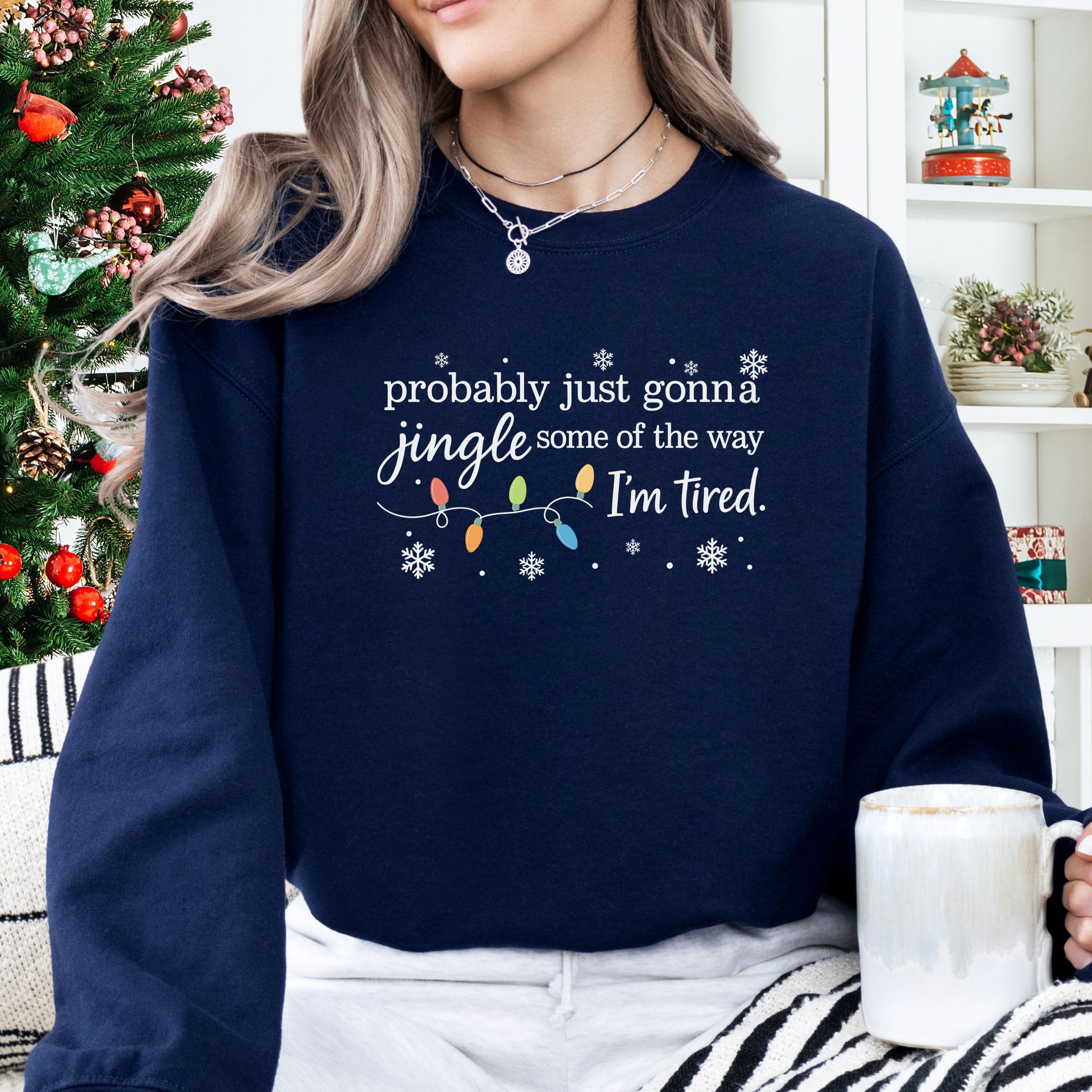 Person wearing a navy sweatshirt with Christmas lights and the text "probably just gonna jingle some of the way I'm tired".