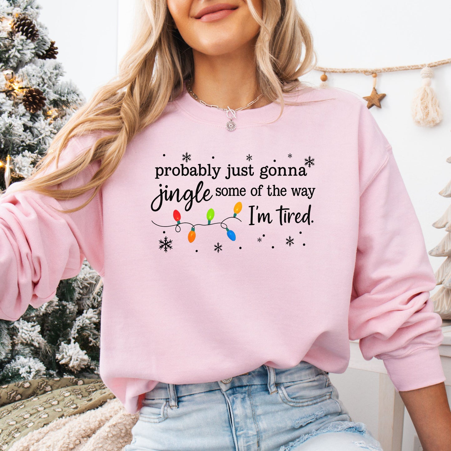 Person wearing a pink sweatshirt with Christmas lights and the text "probably just gonna jingle some of the way I'm tired".