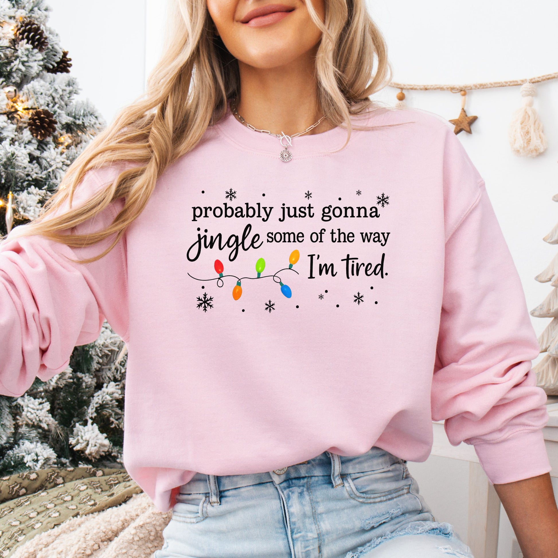 Person wearing a pink sweatshirt with Christmas lights and the text "probably just gonna jingle some of the way I'm tired".