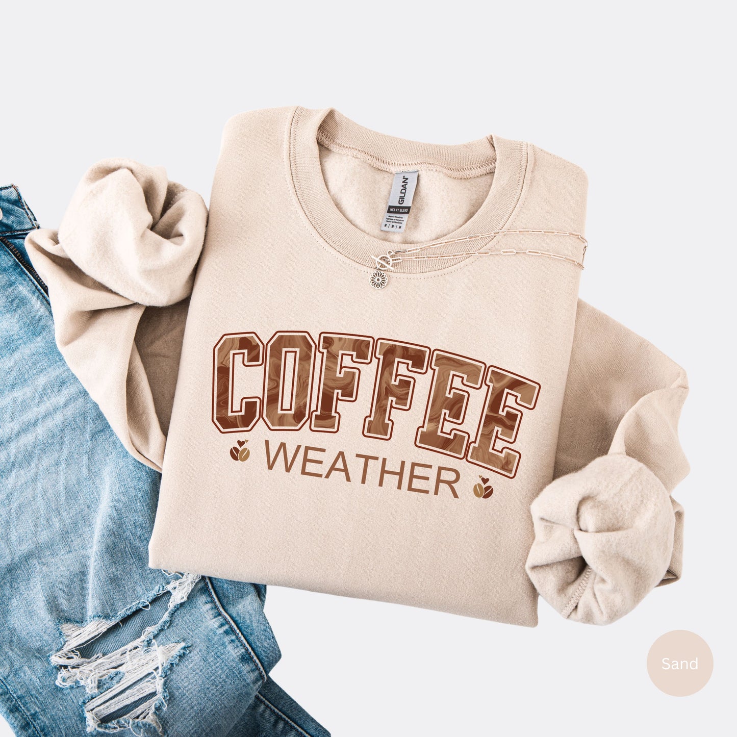Coffee weather sweatshirt with marbled brown lettering and coffee bean icons on sand crewneck.
