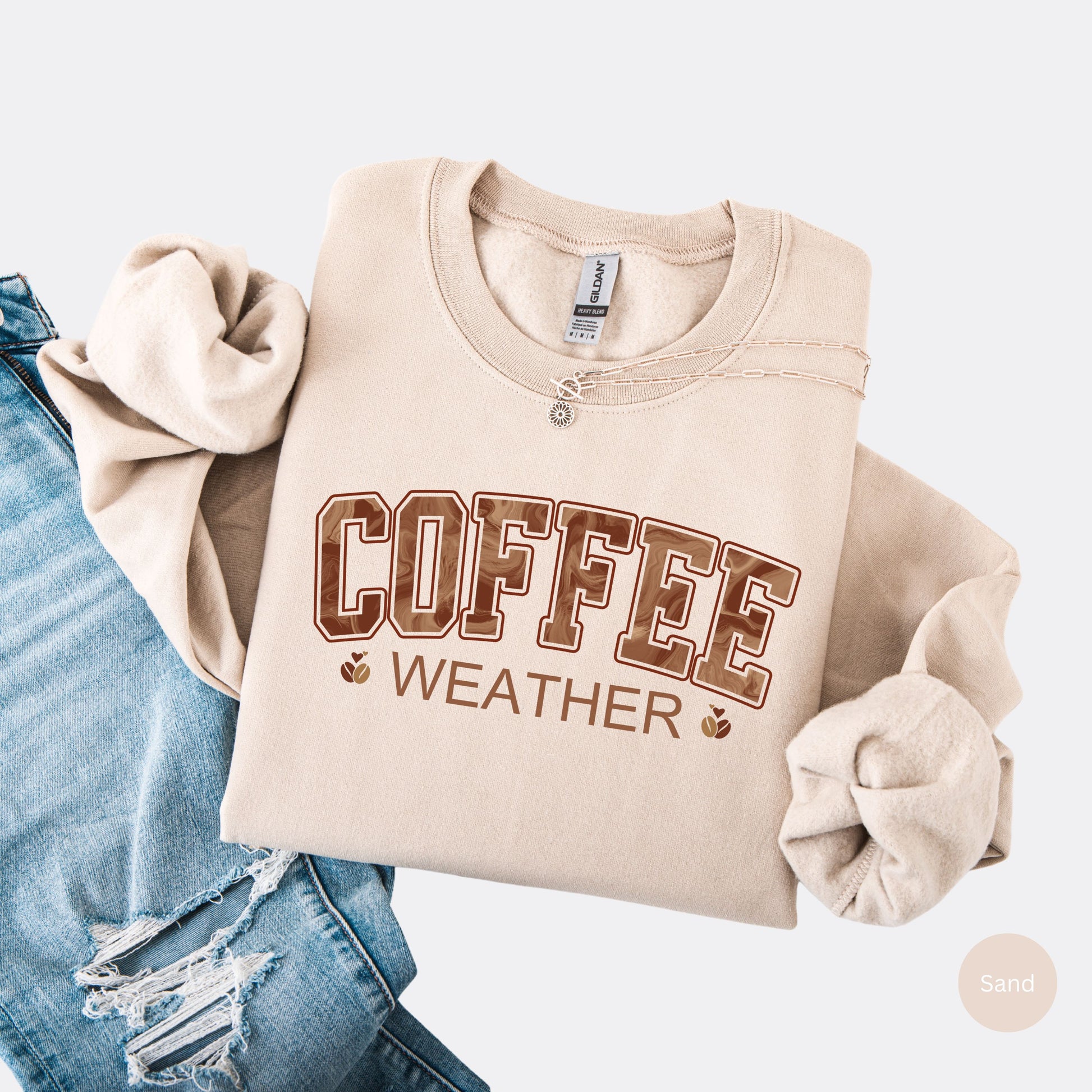 Coffee weather sweatshirt with marbled brown lettering and coffee bean icons on sand crewneck.