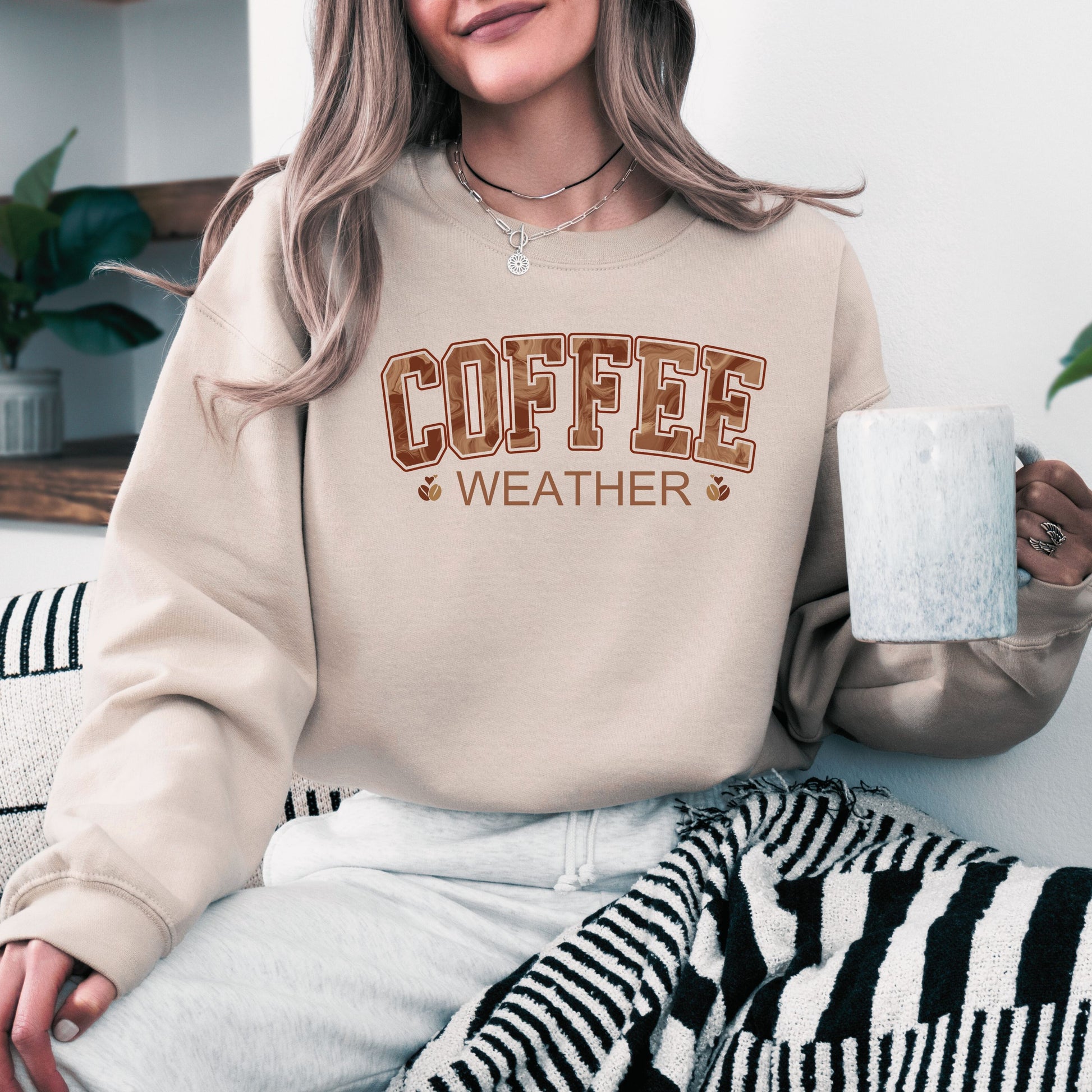 Person wearing coffee weather sweatshirt with marbled brown lettering and coffee bean icons on sand  crewneck.