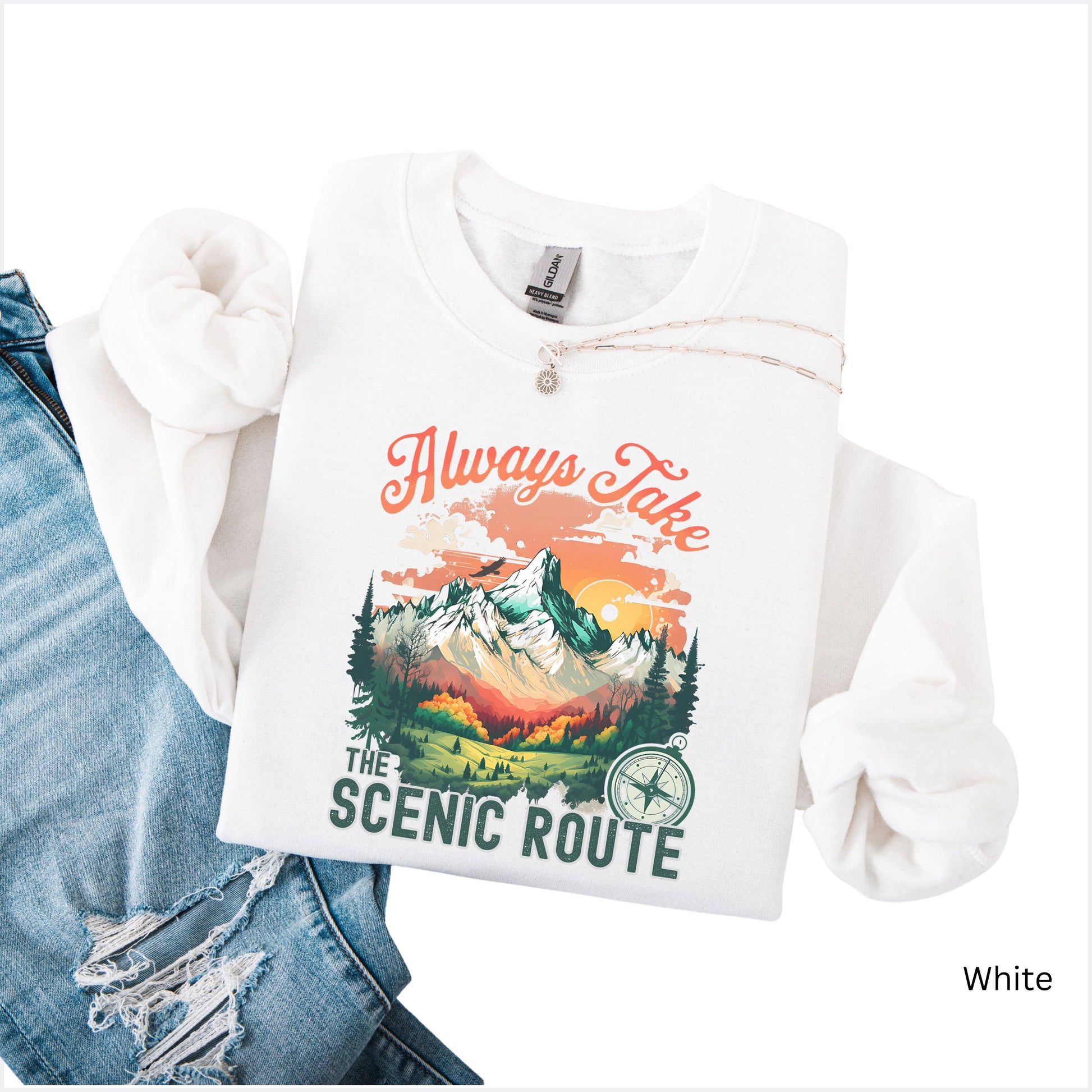Crewneck sweatshirt in the color white with the phrase “Always Take the Scenic Route” and a mountain-inspired graphic on the front.