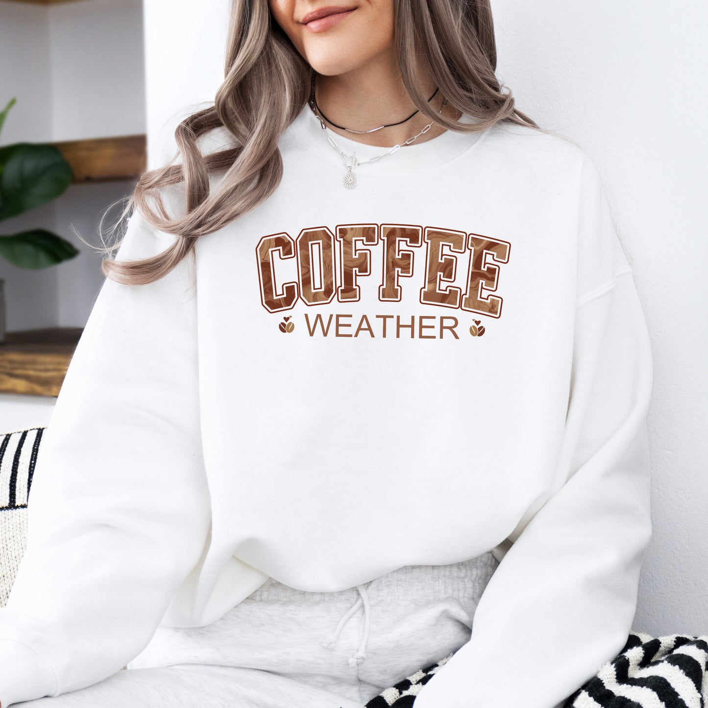 Person wearing coffee weather sweatshirt with marbled brown lettering and coffee bean icons on white crewneck.